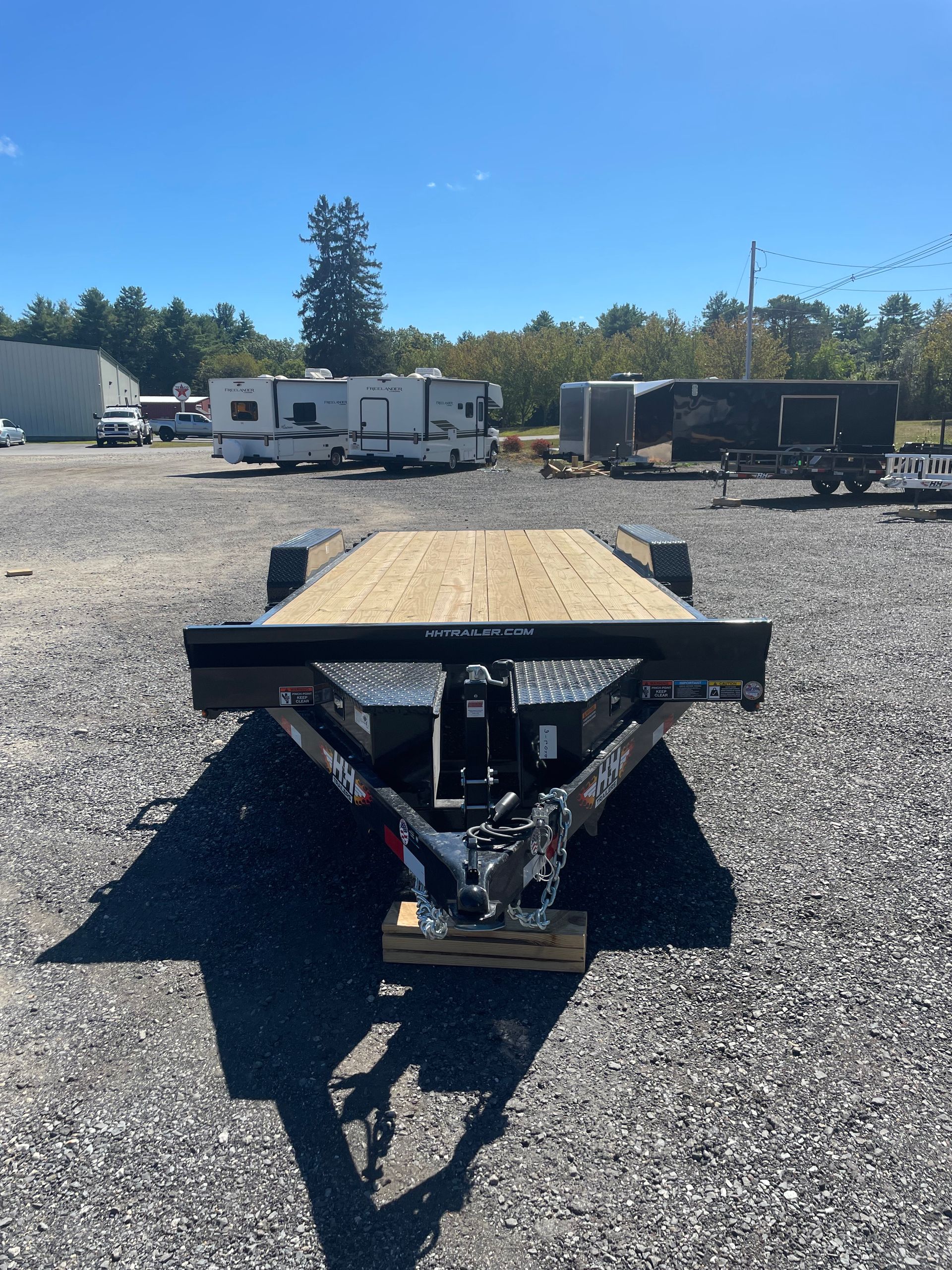Flatbed trailer on gravel, sunny day, with other vehicles in the background.