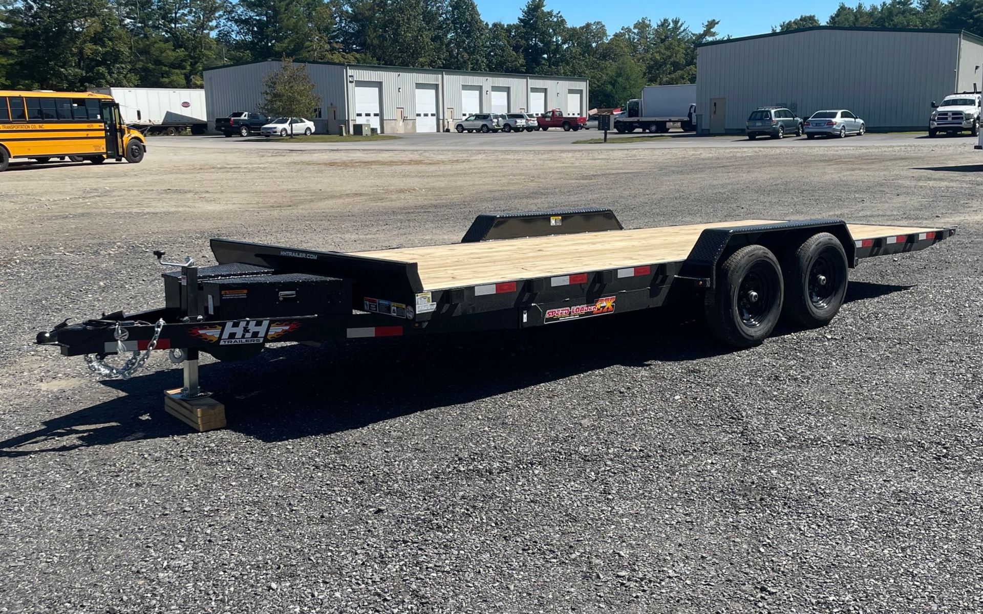 Black flatbed trailer with wooden deck, parked on gravel.