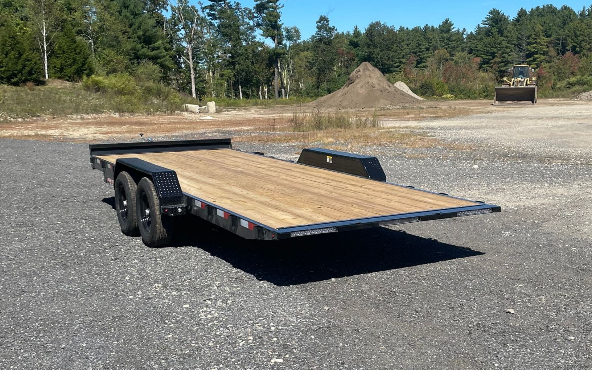 Black flatbed trailer on gravel, with a wooden deck.