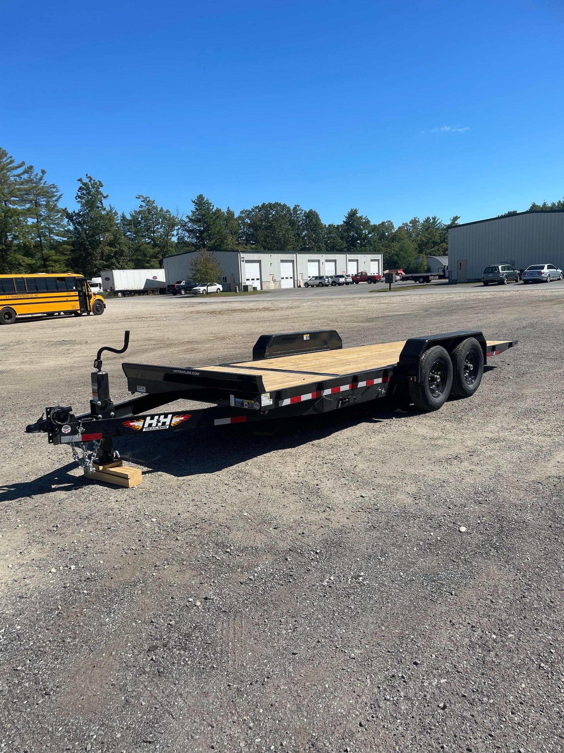 Black flatbed trailer parked on gravel, with a blue sky background.