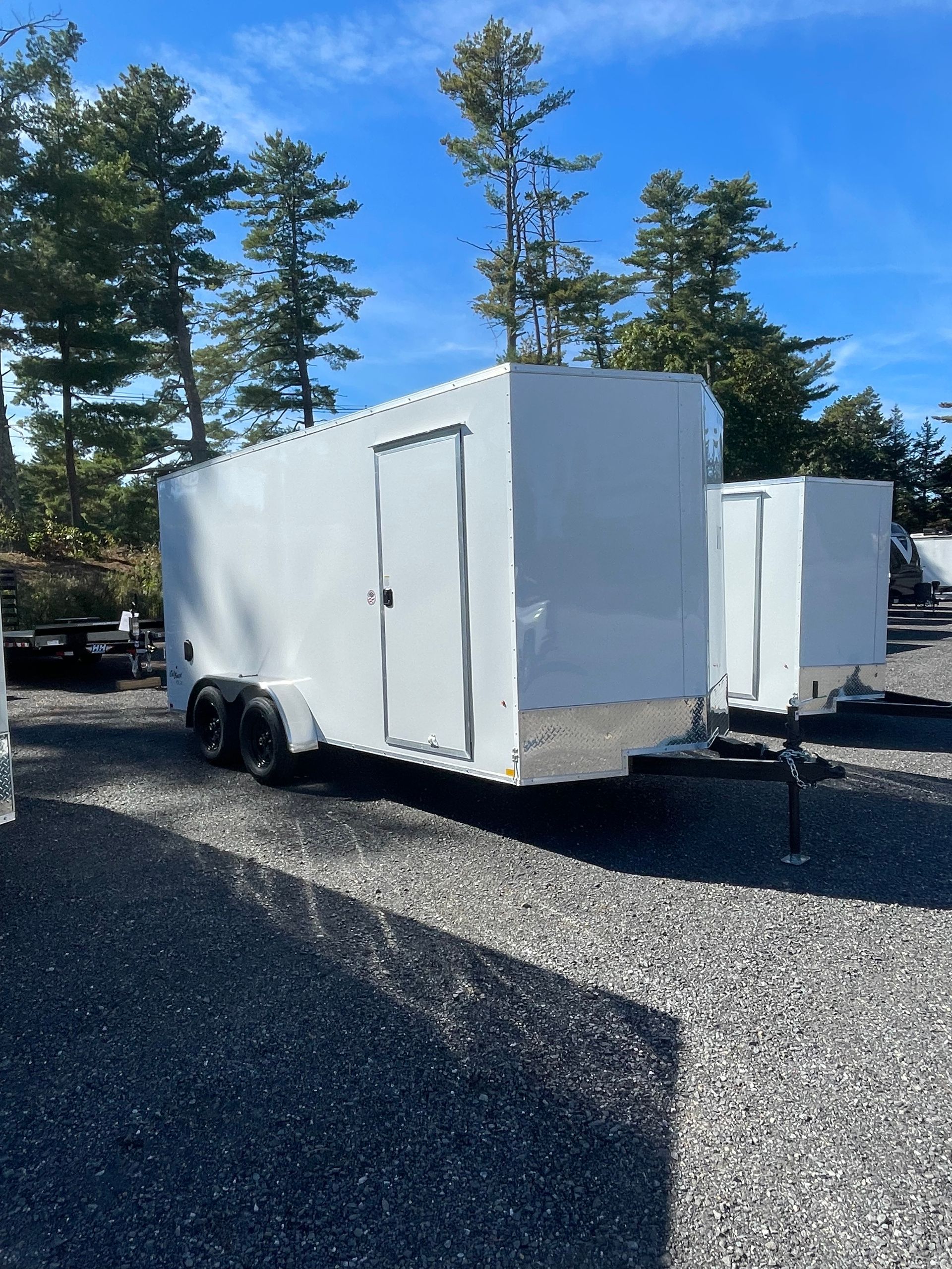 White enclosed cargo trailer on a gravel lot under a blue sky.