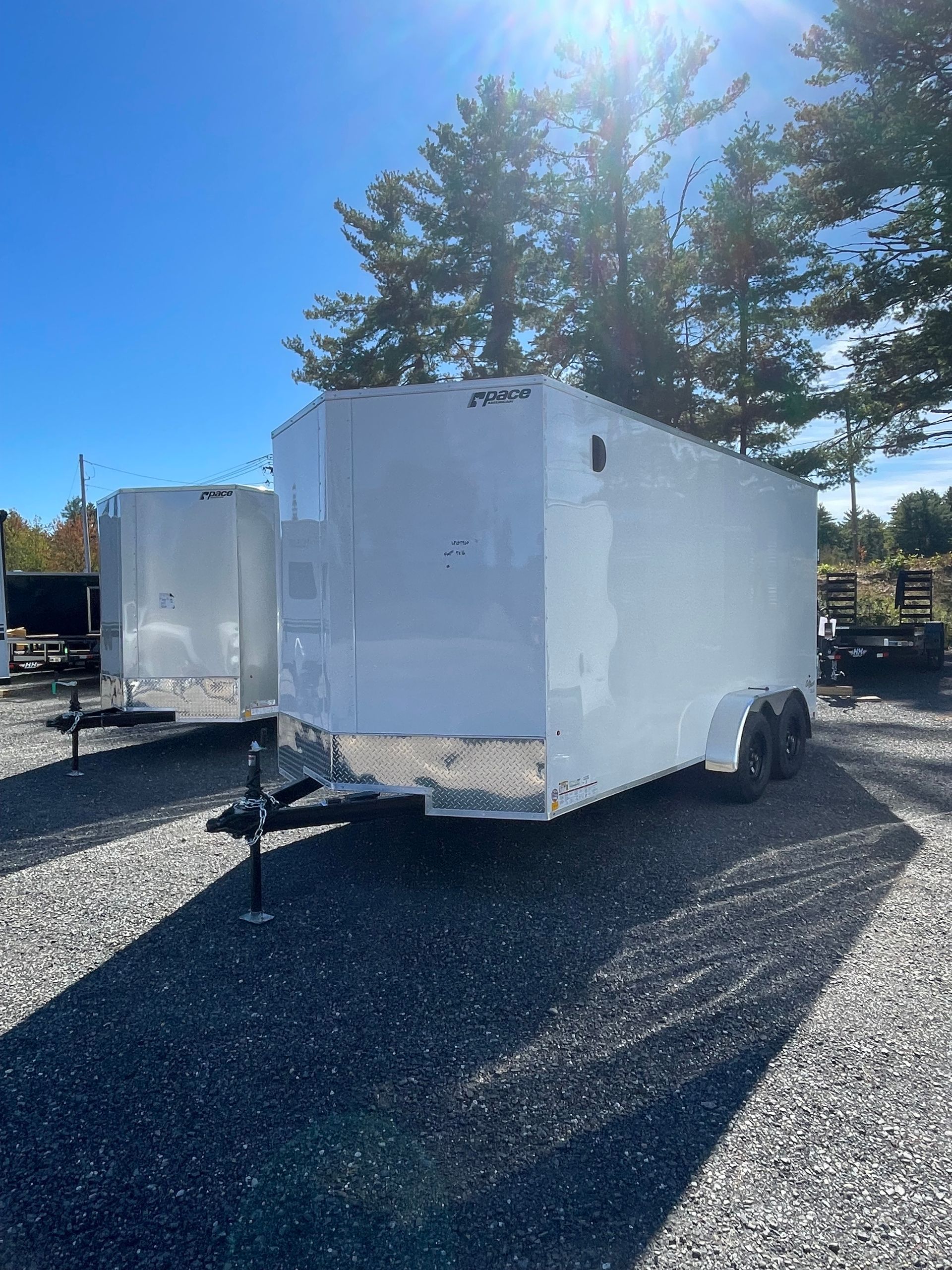 White enclosed cargo trailer, parked outdoors on gravel, sunny day.