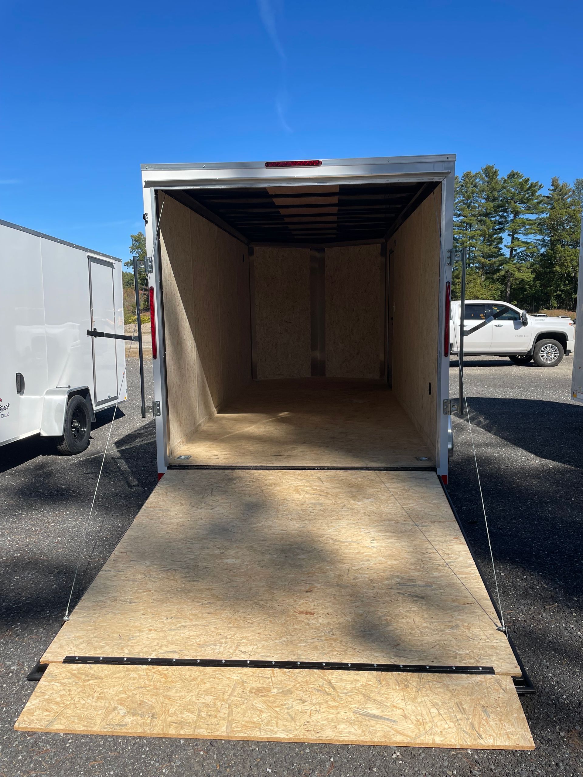 Open cargo trailer with a ramp, empty interior, parked outside on a sunny day.