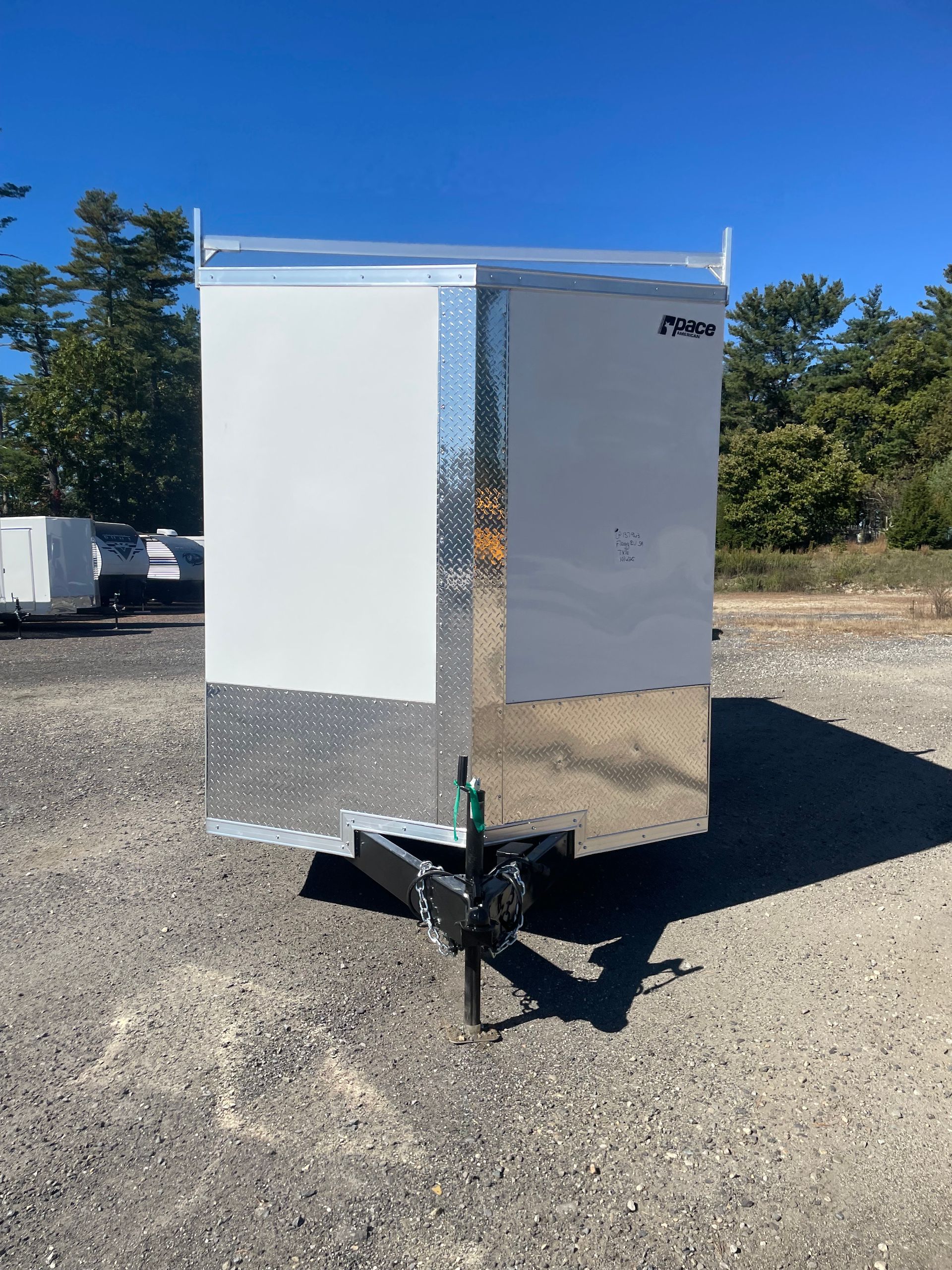 White and silver enclosed trailer parked on gravel under a blue sky.