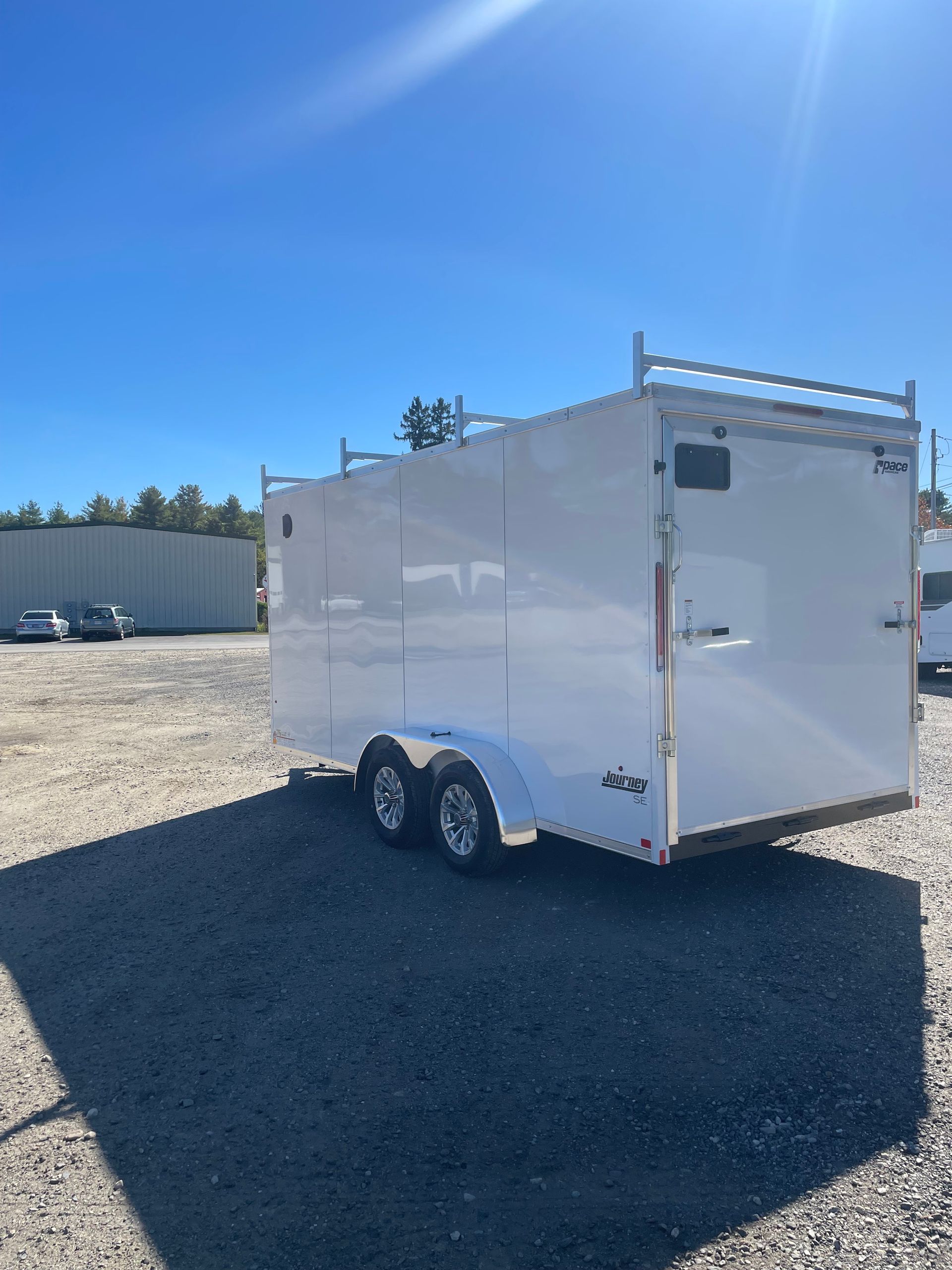 White enclosed trailer with ladder racks, parked outside on a sunny day.