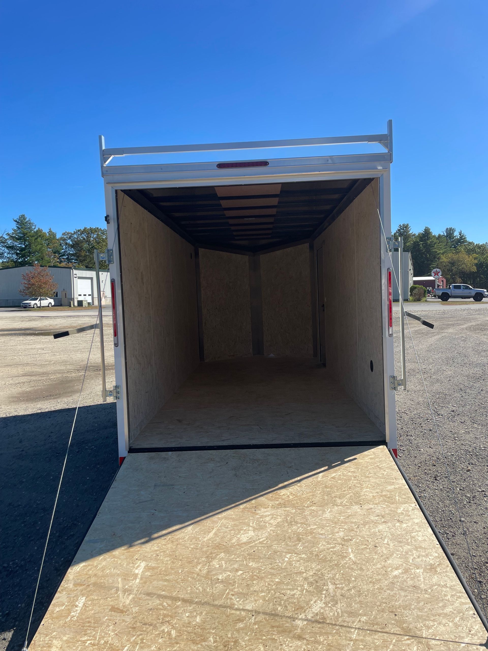 An empty cargo trailer with open ramp, showing light-colored plywood interior against a blue sky background.