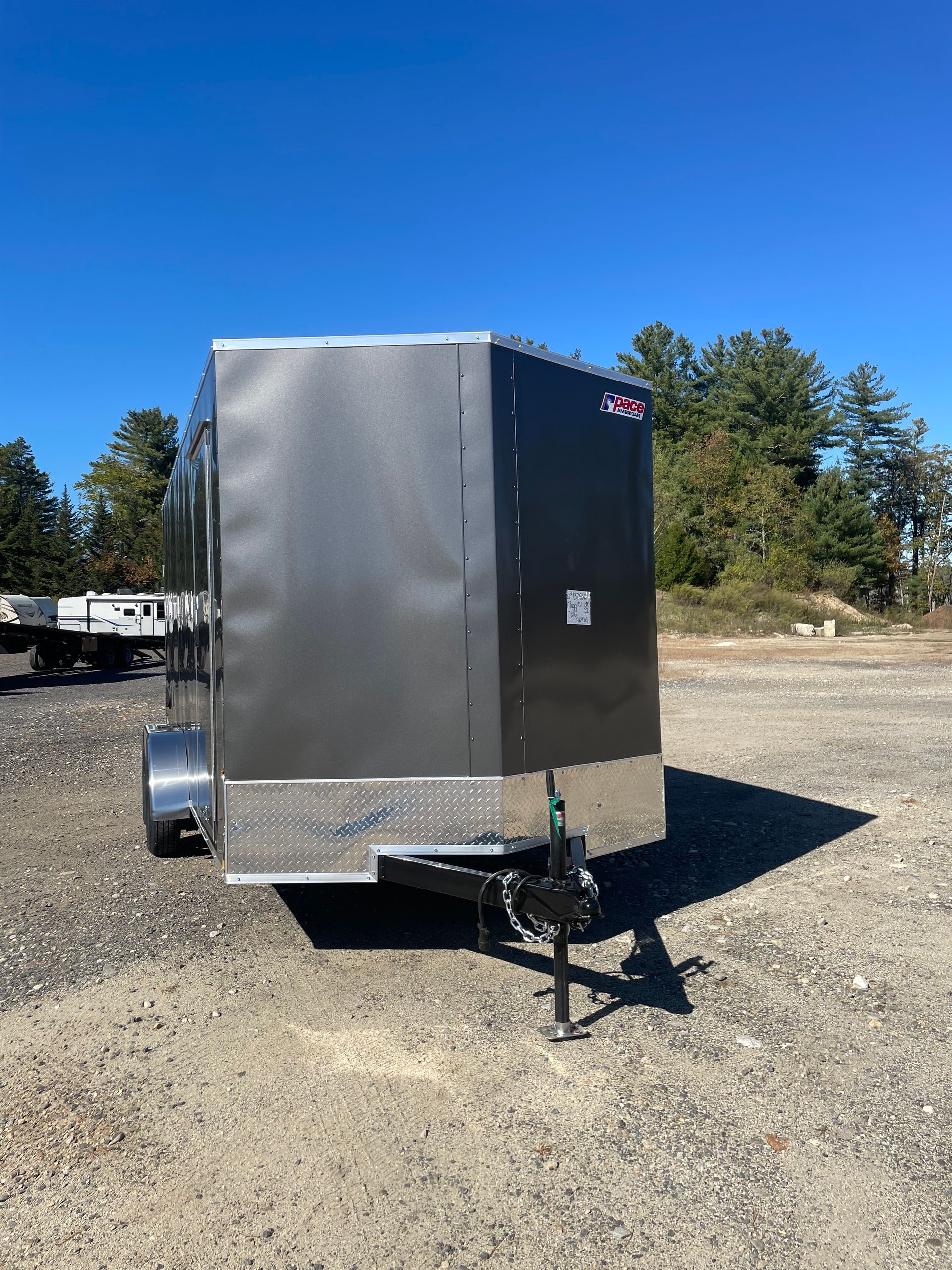 Dark gray enclosed cargo trailer on a gravel lot under a clear blue sky.