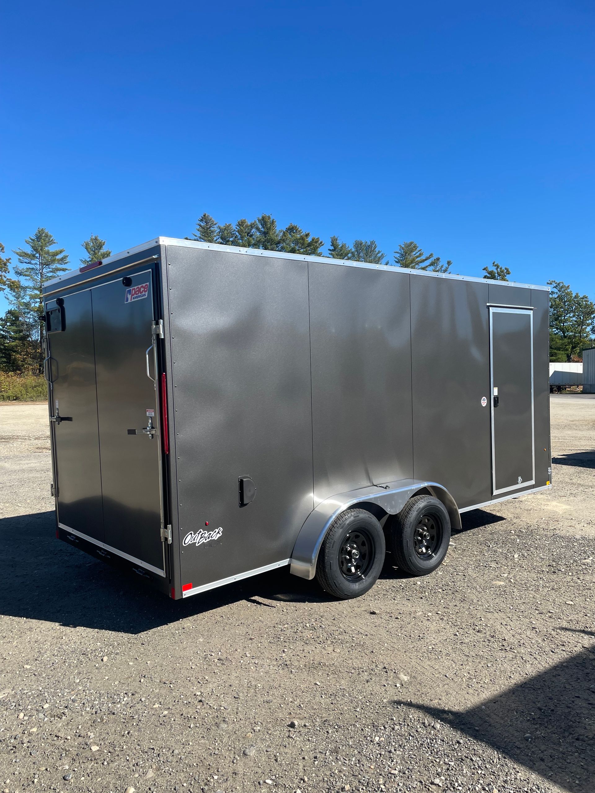 Gray enclosed cargo trailer parked outdoors on gravel.