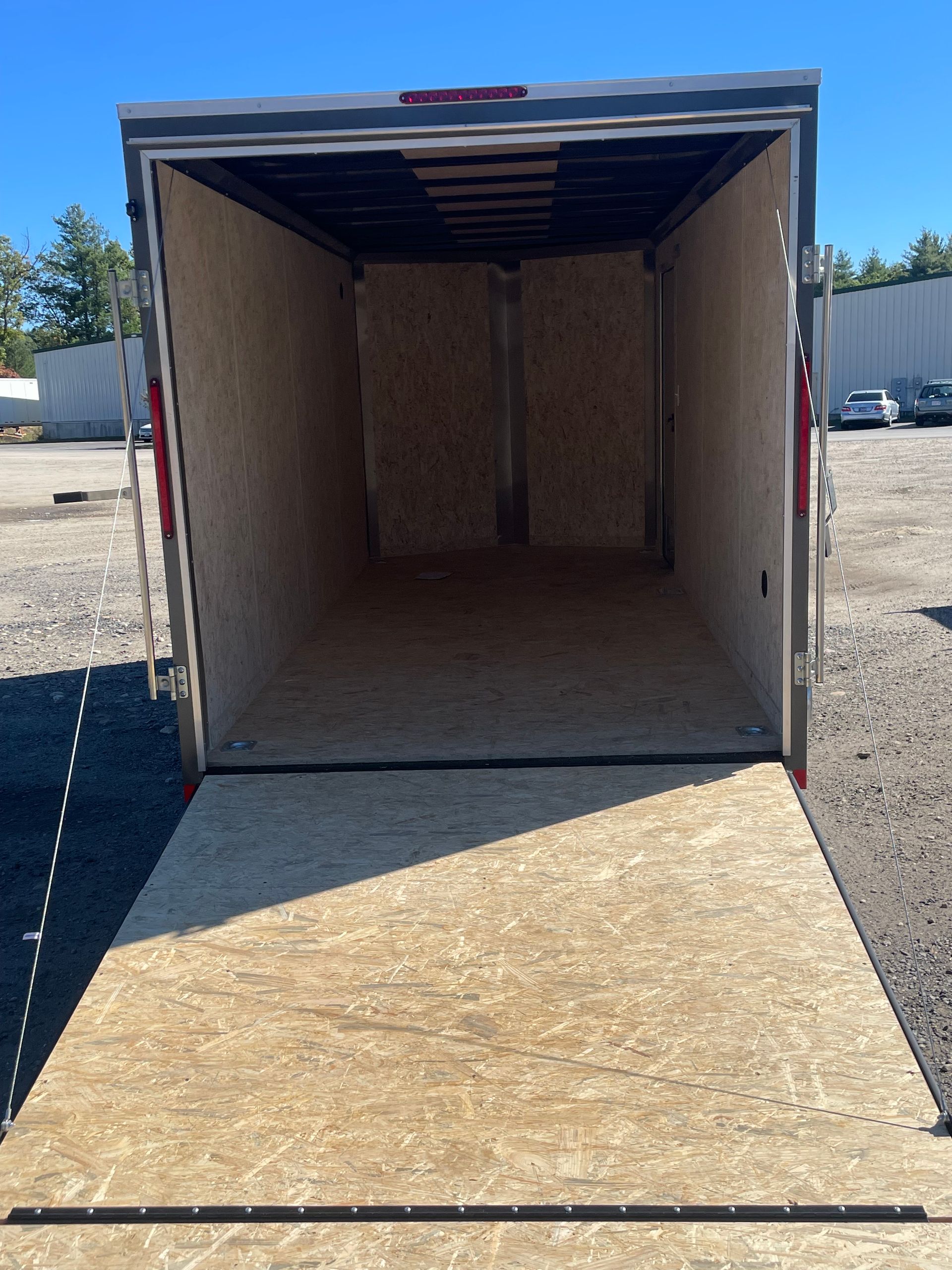 Empty cargo trailer with a wooden floor and open ramp, outdoors on a sunny day.