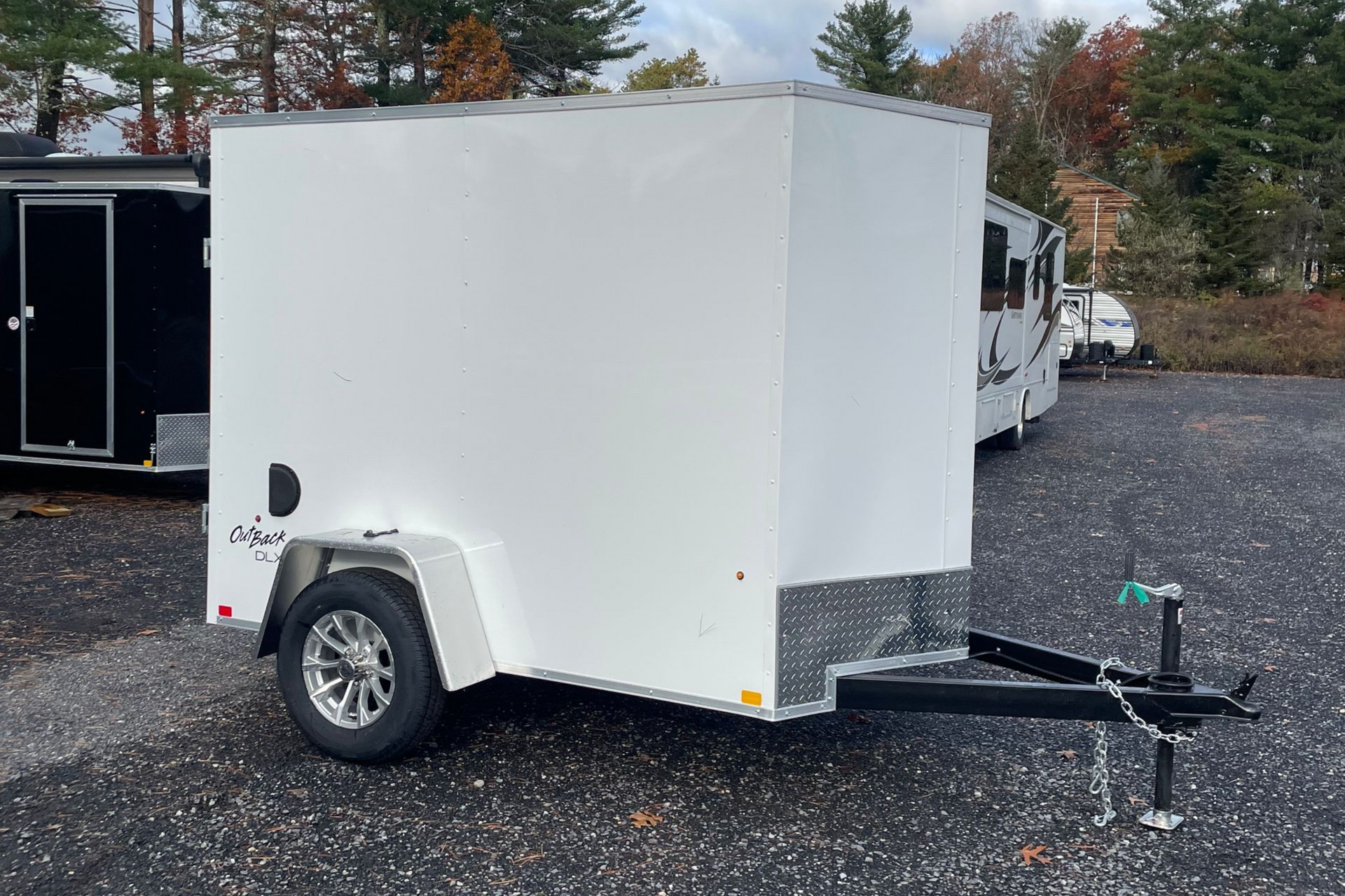White enclosed cargo trailer with a black hitch and wheel, parked outside.