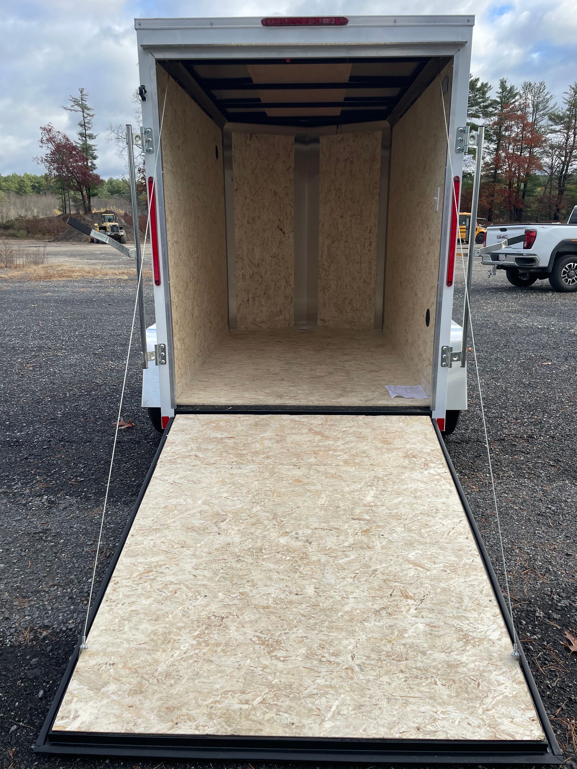 Open white cargo trailer with ramp extended, parked on gravel.