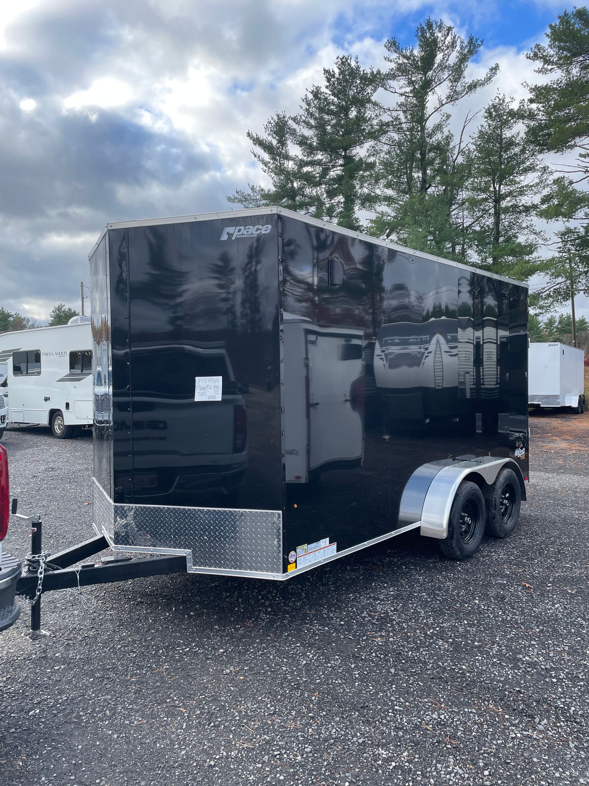 Black enclosed trailer with side door and black wheels parked outside on a cloudy day.