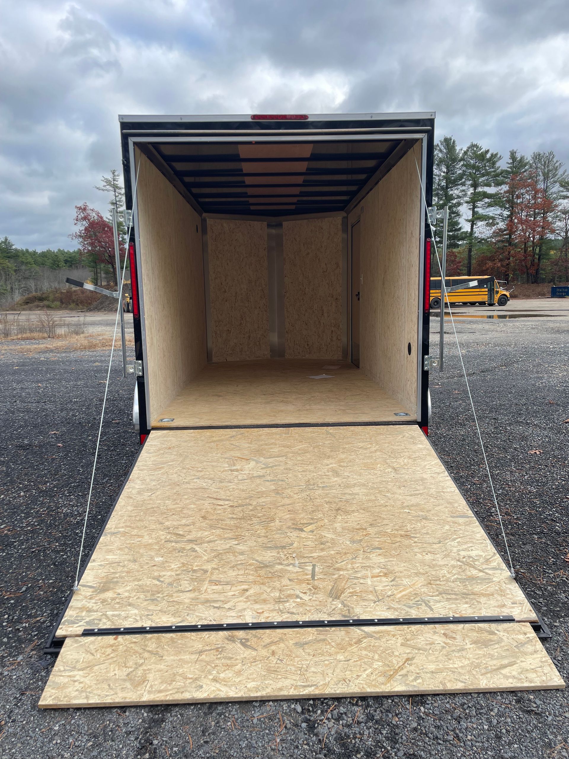 Empty cargo trailer with a ramp down on gravel. Interior walls are wood.