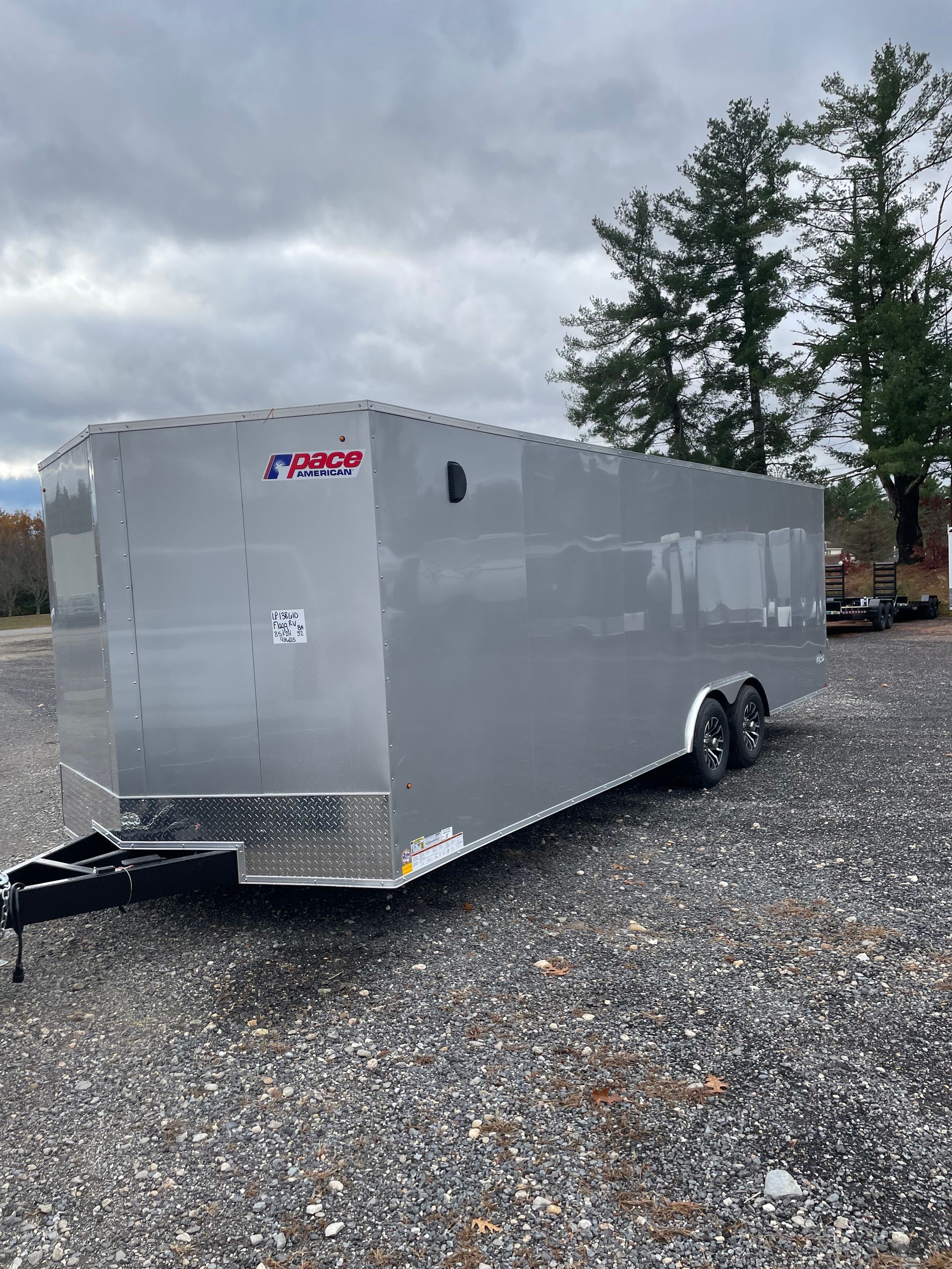 Silver enclosed trailer parked on gravel under a cloudy sky.