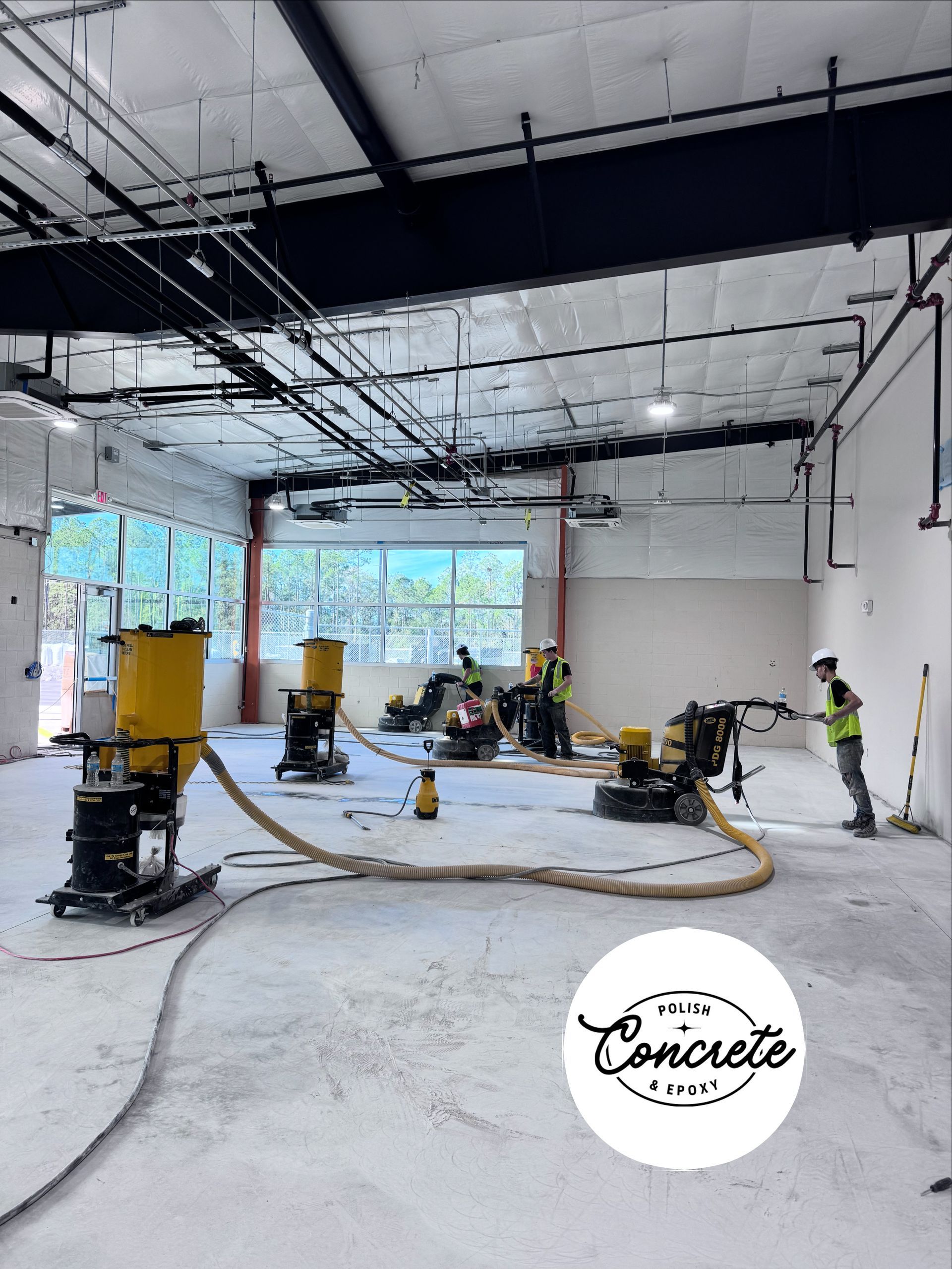Construction crew smoothing a concrete floor inside a large unfinished building with hoses and equipment
