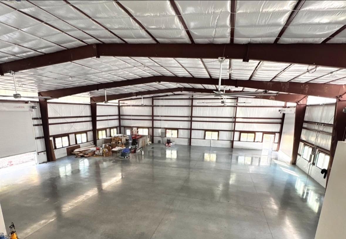 Empty warehouse interior with concrete floor, metal beams, and storage items along the left wall