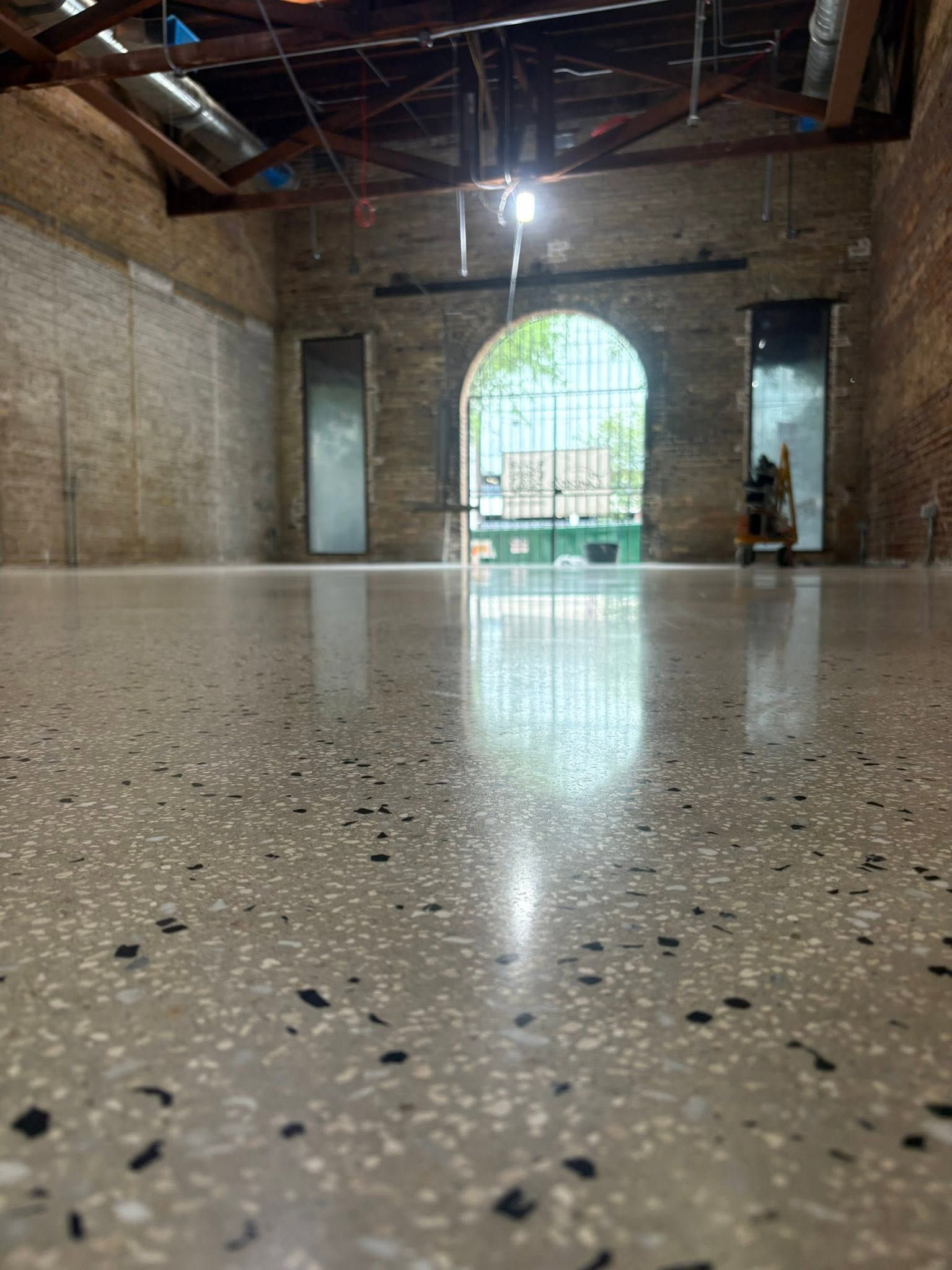 Empty brick hall with a glossy speckled floor and a large arched doorway letting in daylight.