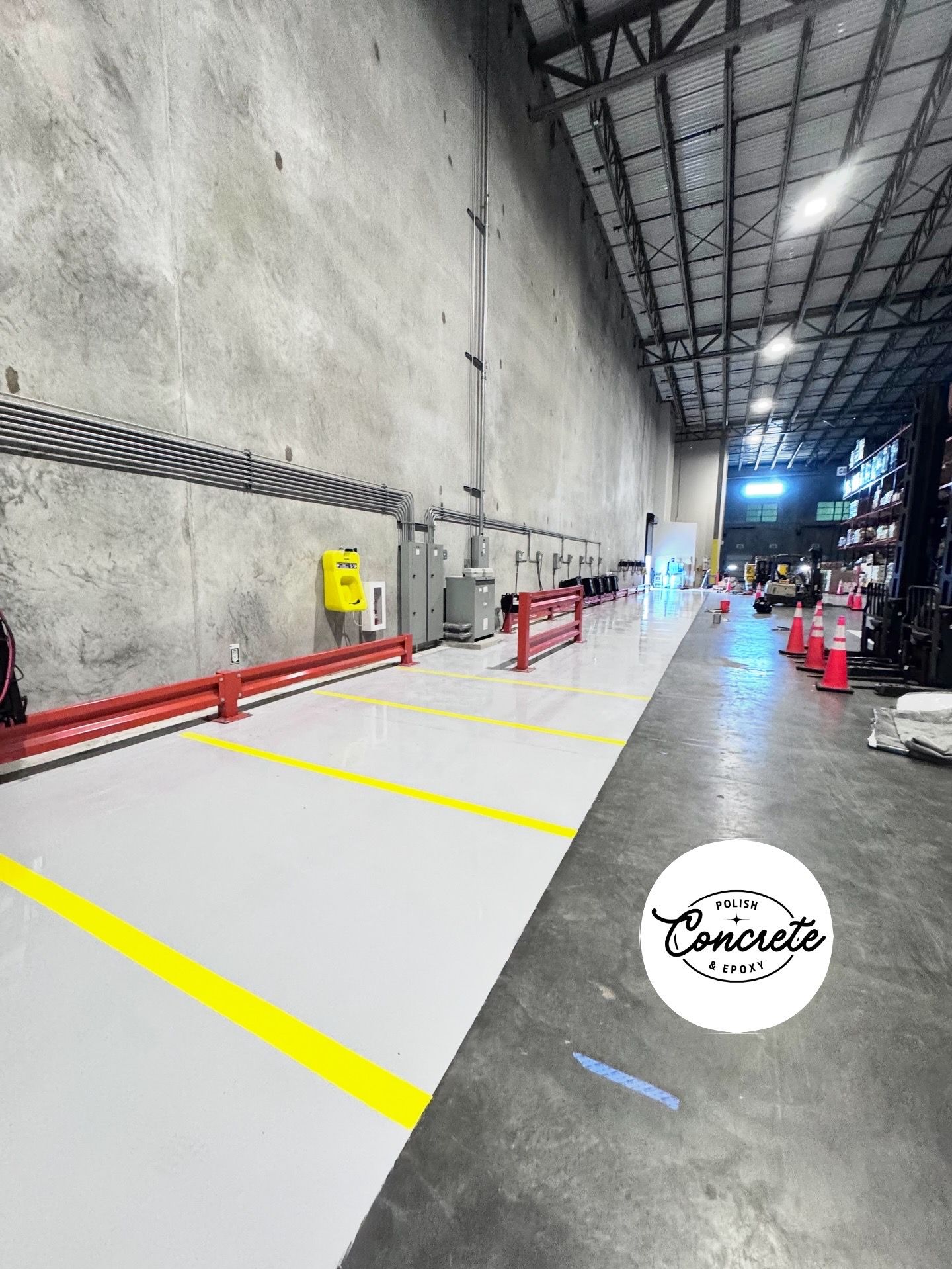 Warehouse aisle with red railings, yellow floor markings, and stacked equipment under bright overhead lights