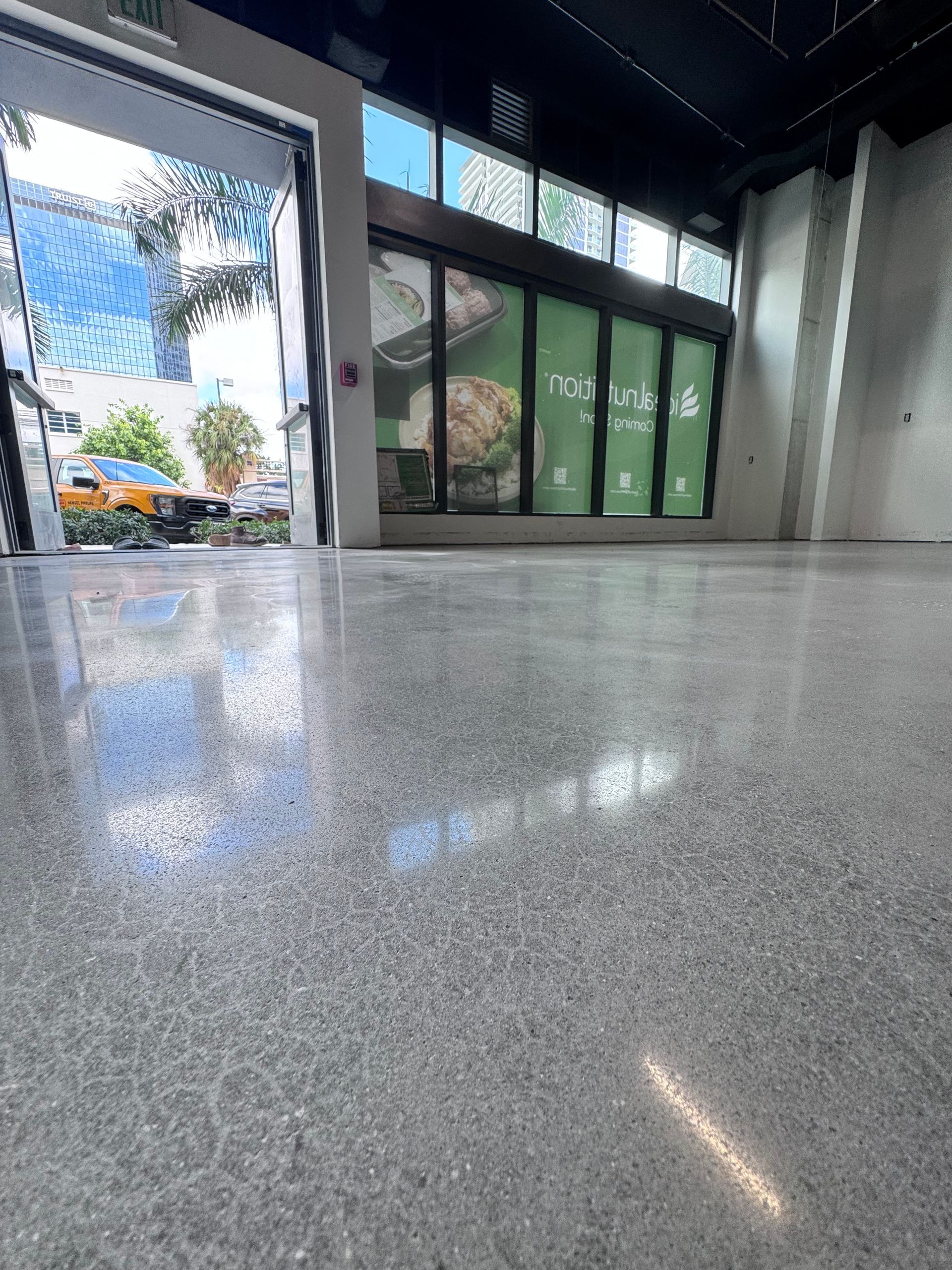 Empty indoor lobby with polished gray floor and glass doors opening to greenery outside