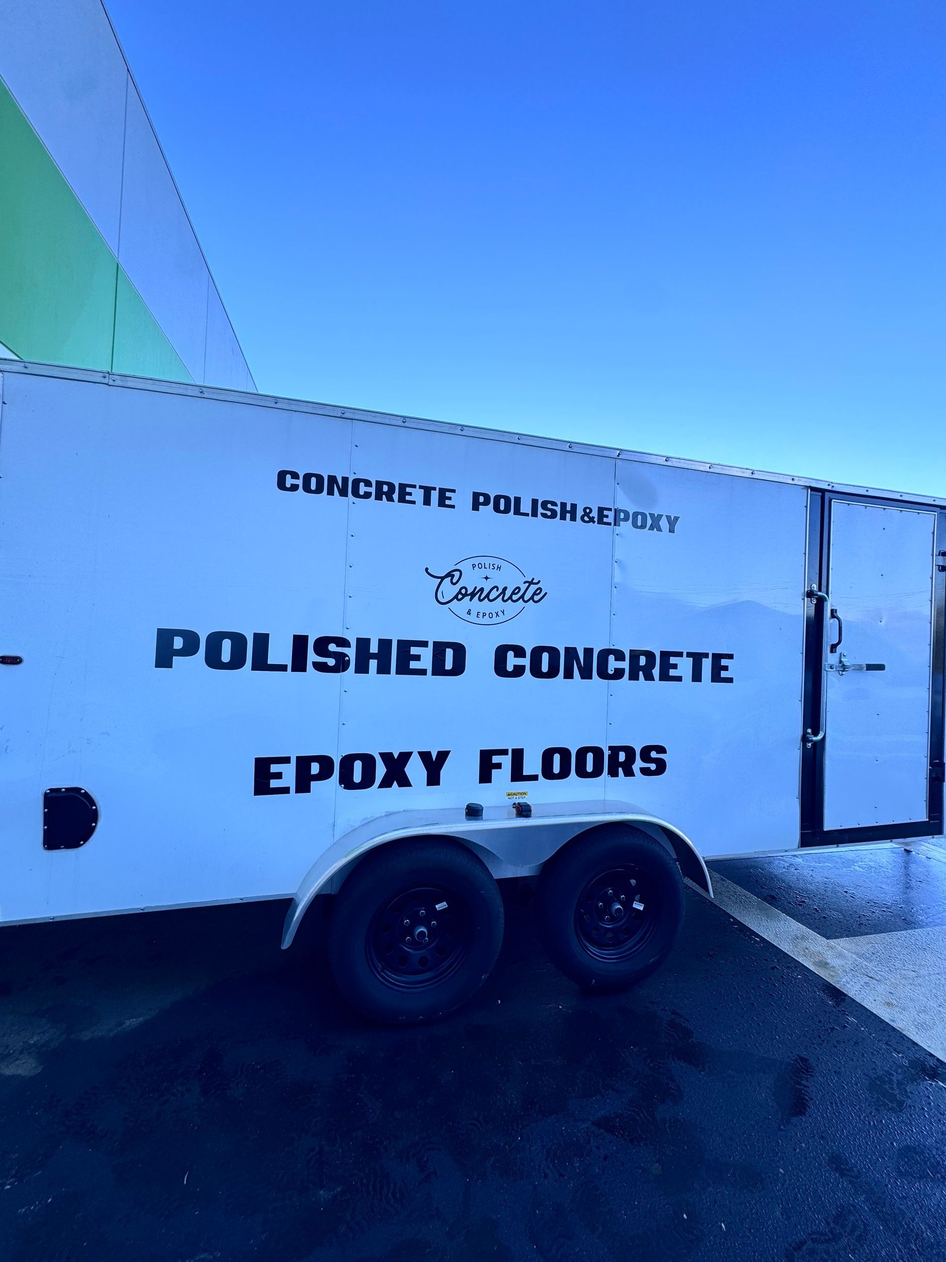 Trailer with white sign reading “Polished Concrete” and “Epoxy Floors” under a blue sky