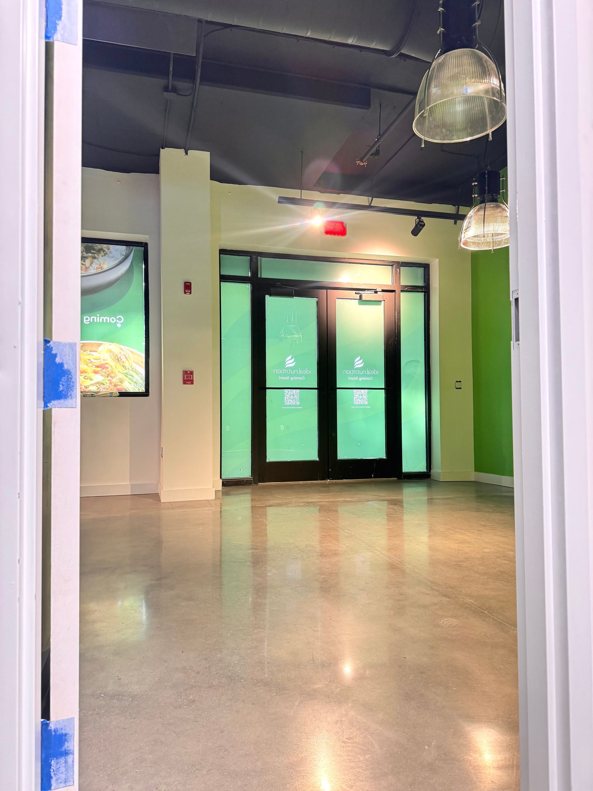 Empty lobby with glass doors, polished floor, and green walls under hanging lights.