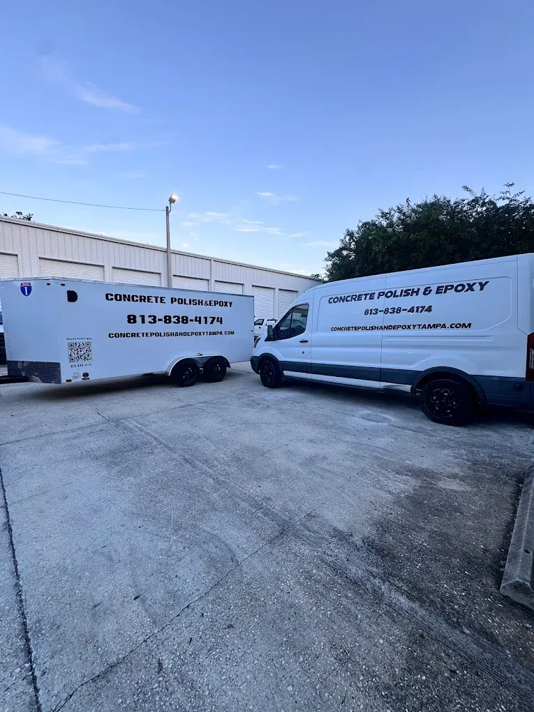 Two white service vans parked in a lot beside a building under a clear blue sky.
