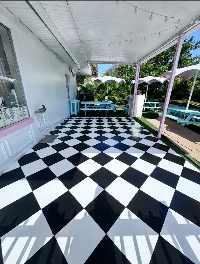Black-and-white checkered porch with turquoise tables, white umbrellas, and string lights overlooking greenery