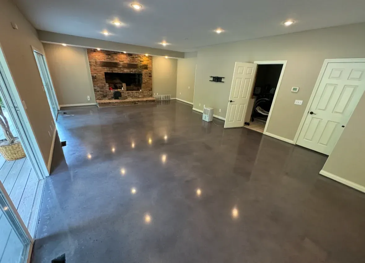 Empty living room with gray floor, recessed lights, and a stone fireplace on the far wall.