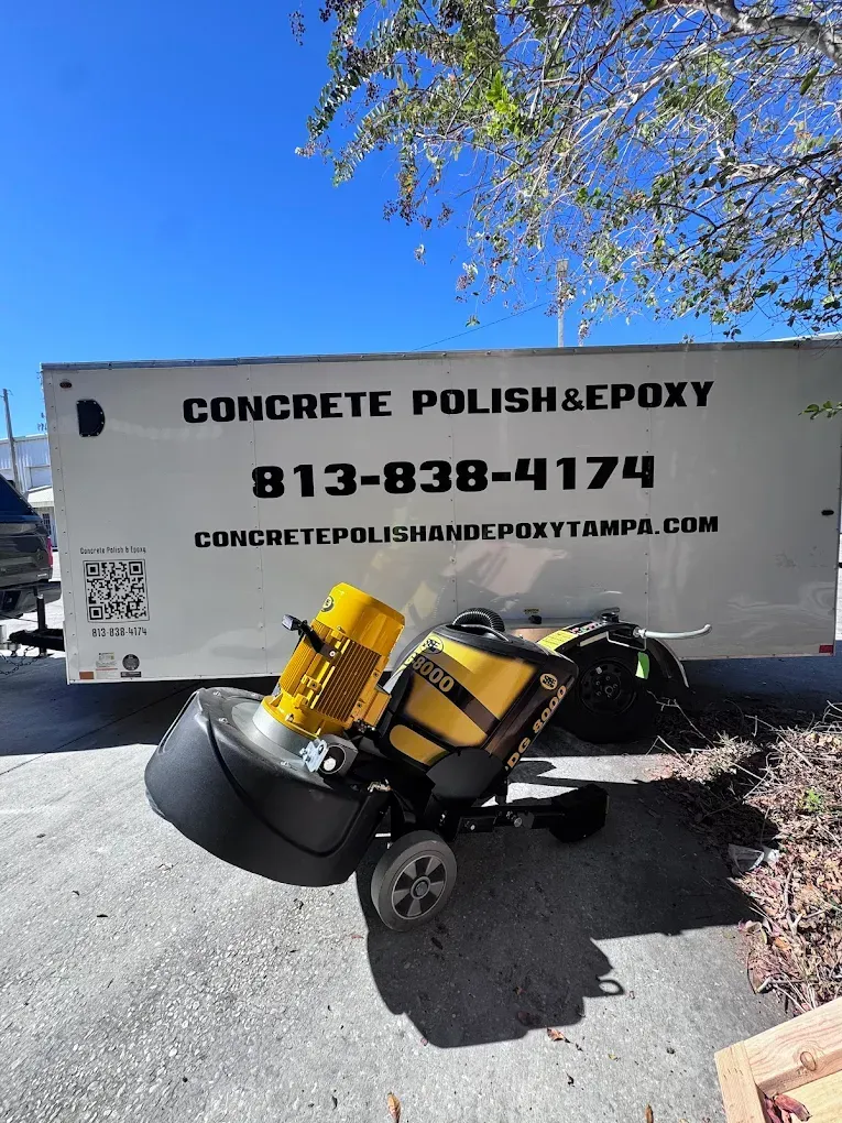 Concrete Polish & Epoxy trailer with phone number, carrying yellow floor-polishing equipment on a sunny driveway.
