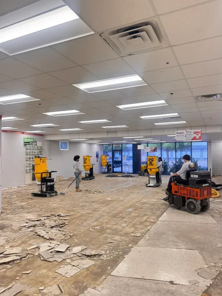 Retail store under renovation, with workers, debris, and floor-cleaning equipment inside.
