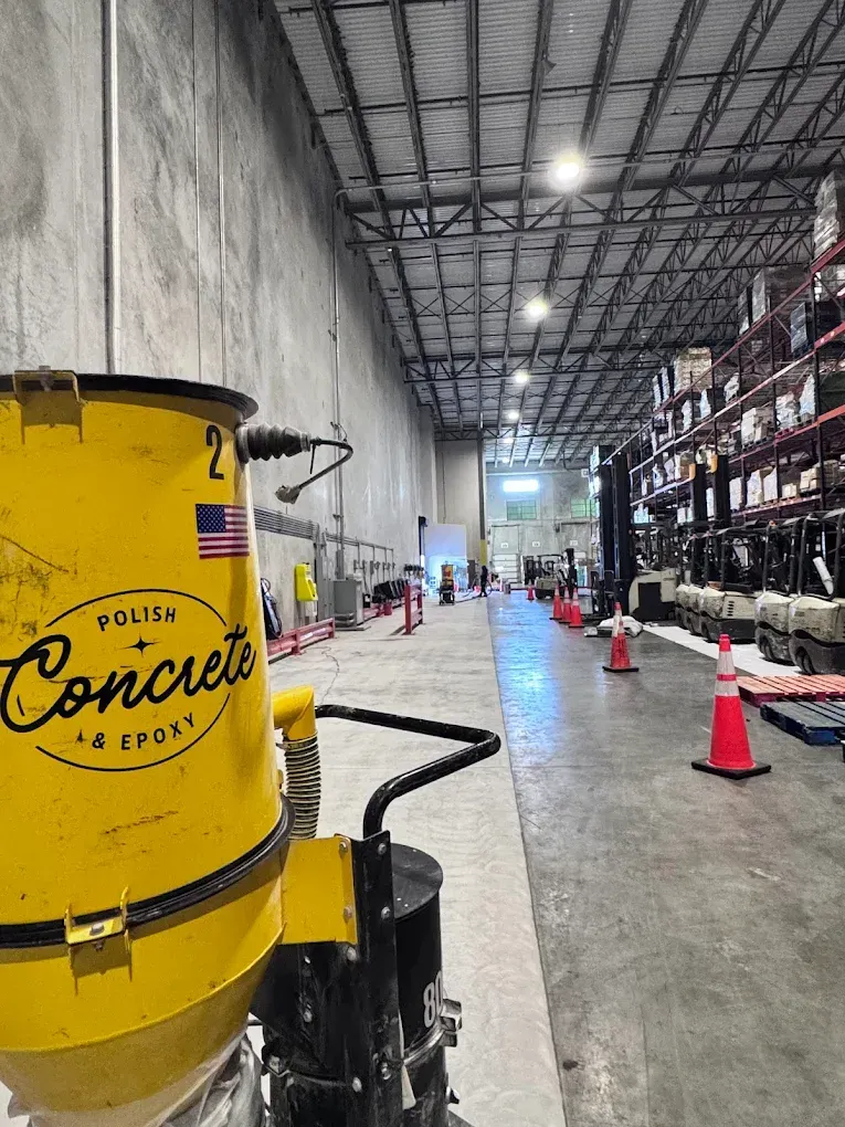 Yellow concrete pump in warehouse aisle with shelves, orange cones, and overhead lights