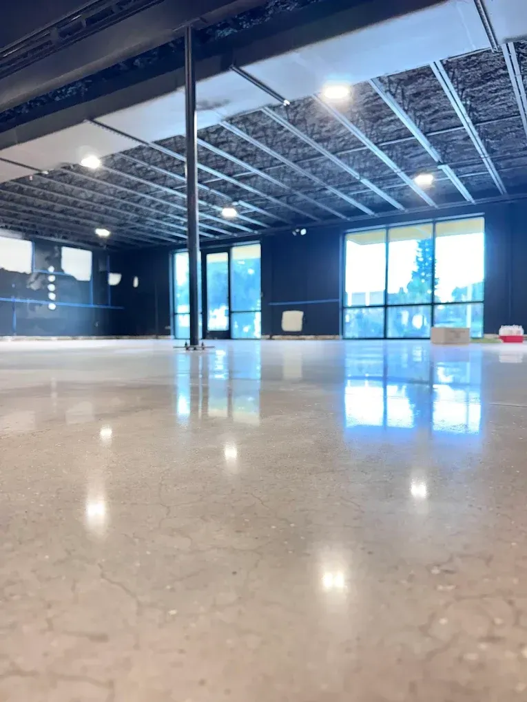 Empty modern room with polished concrete floor, exposed ceiling beams, and large windows.