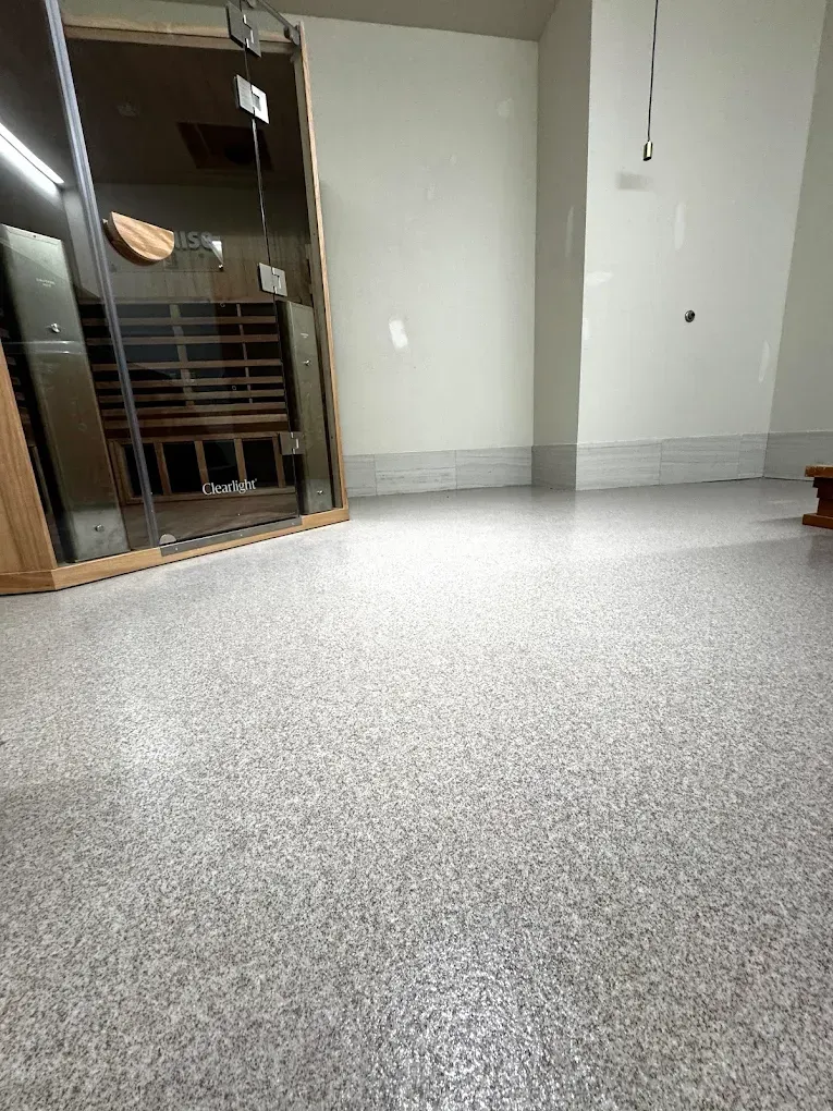 Empty room with speckled floor, white walls, and a wooden glass cabinet by the left wall.
