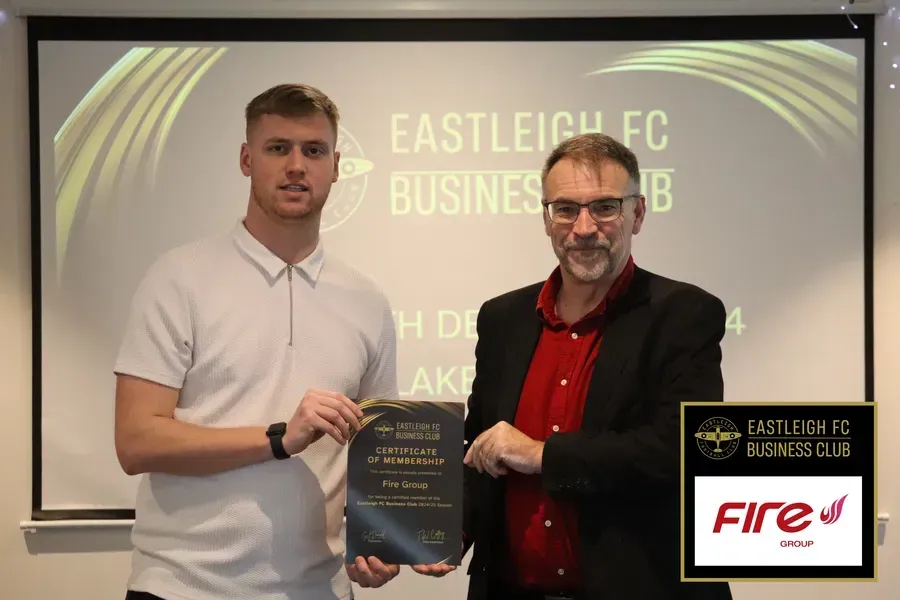 Man receives award from another man, likely at a business event. Eastleigh FC Business Club logo is visible.