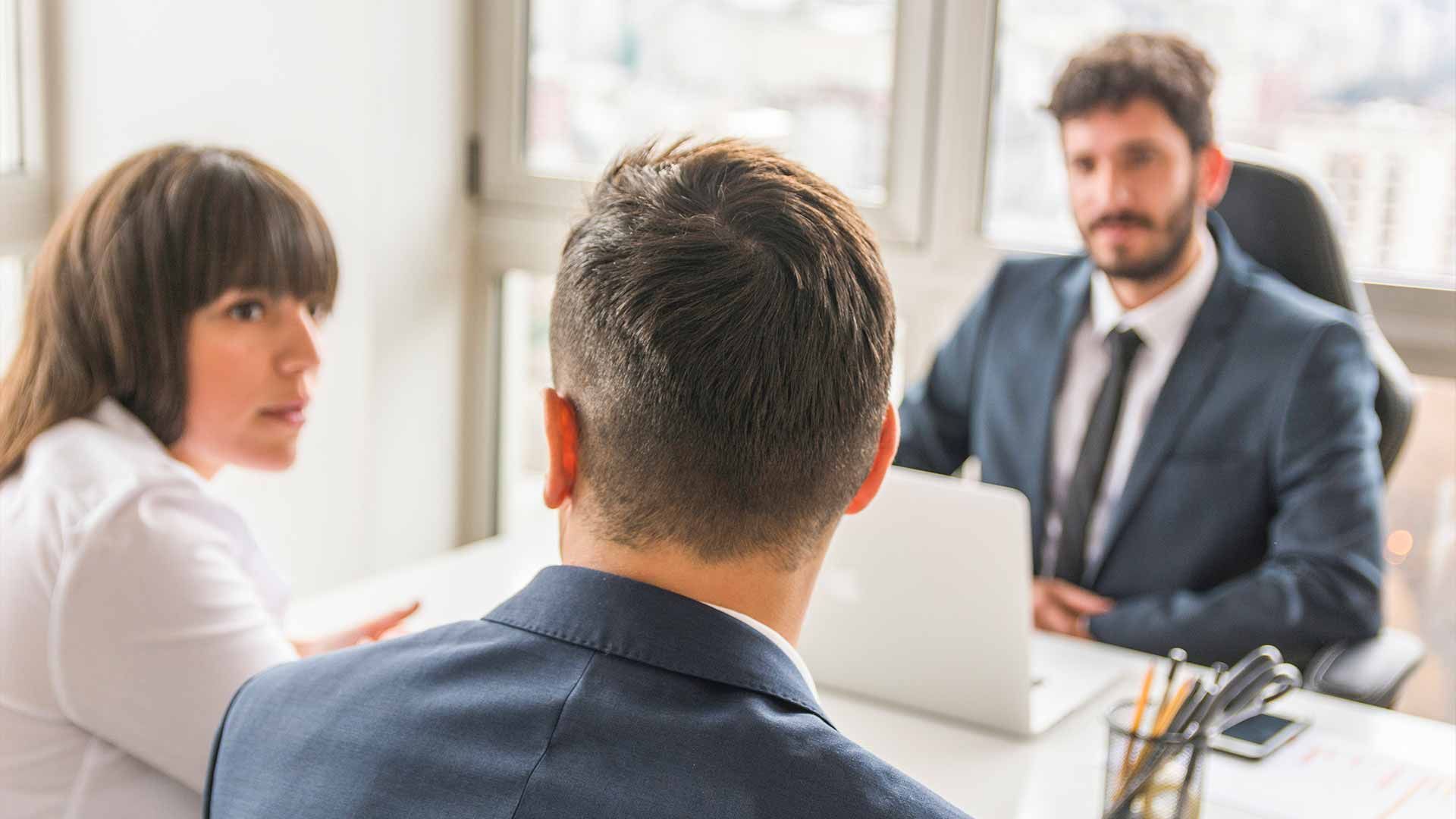 A man in a suit and tie is sitting at a table with two other people.