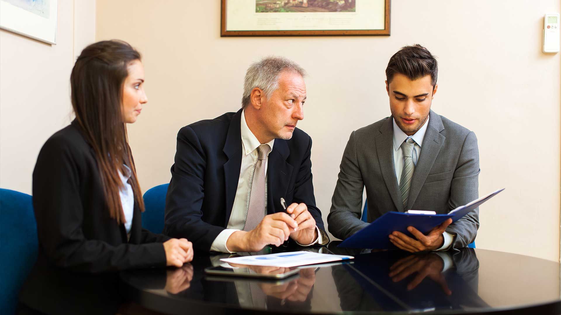 A group of people are sitting around a table looking at a clipboard.