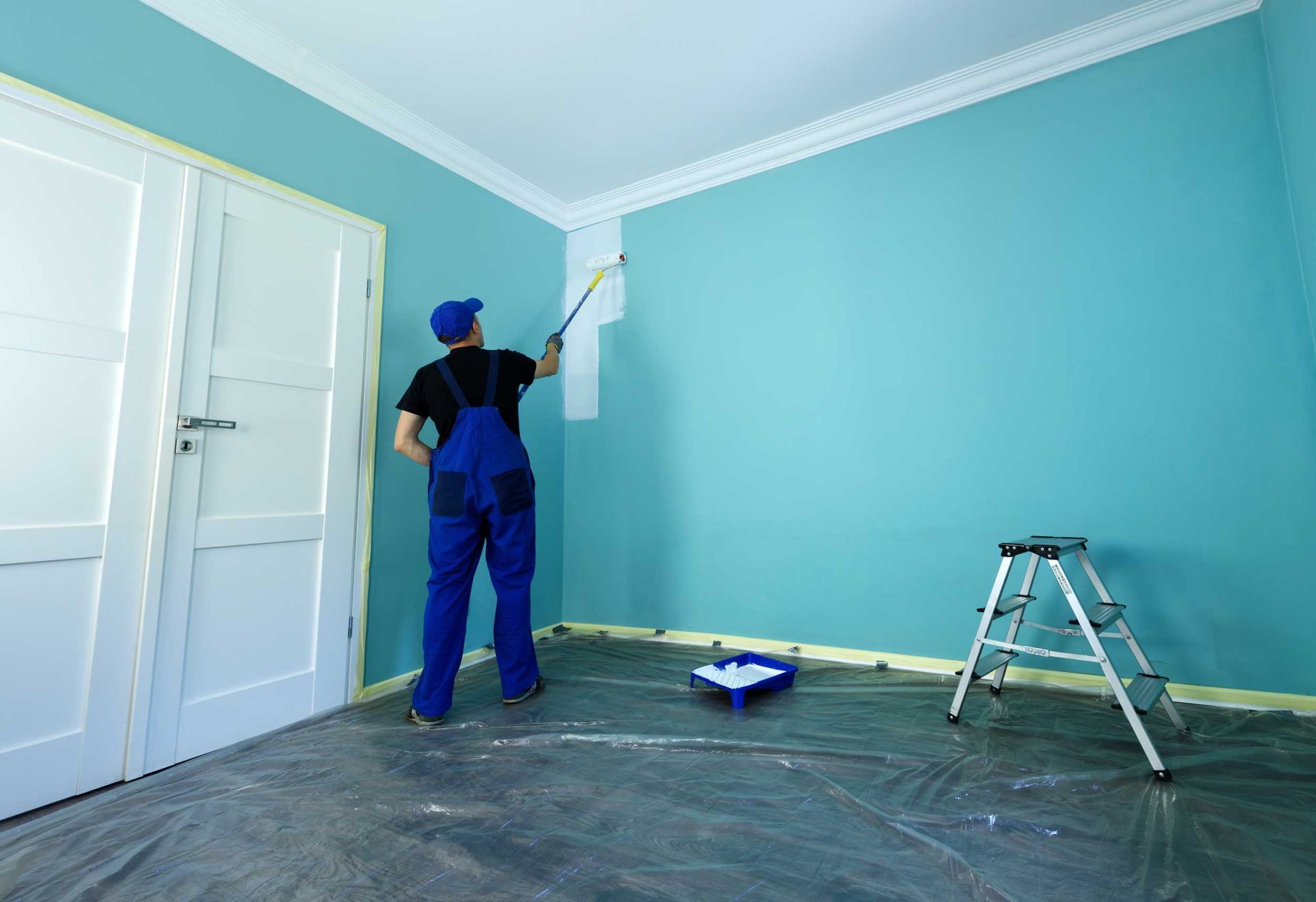 A man in working overalls is painting a wall in white color A man in working overalls is painting a wall in white color