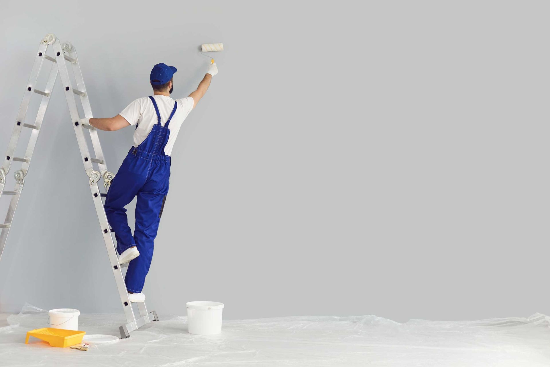 A male painter painting a grey wall with a roller brush
