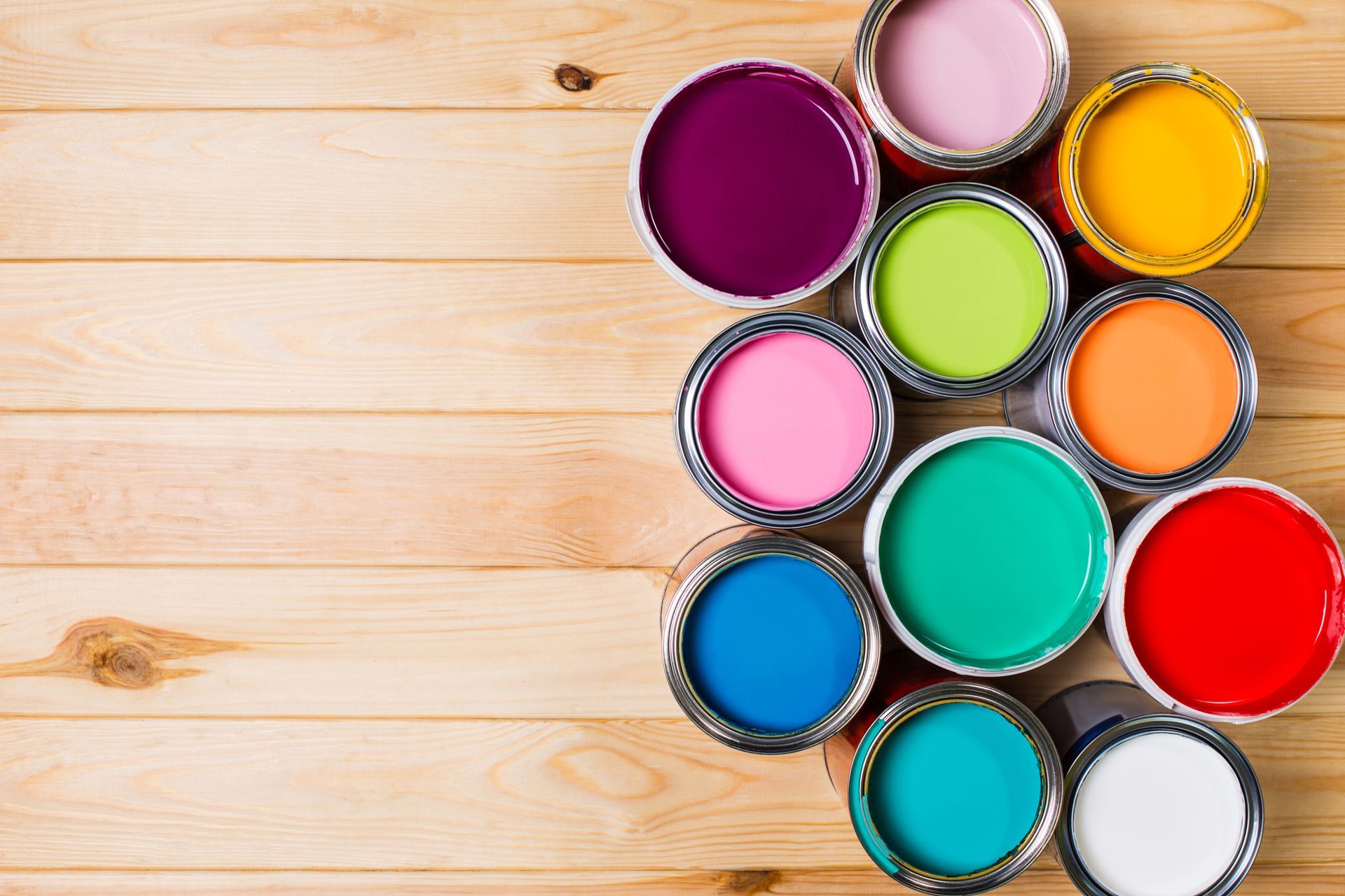 Open paint cans in various colors arranged on a light wood surface.