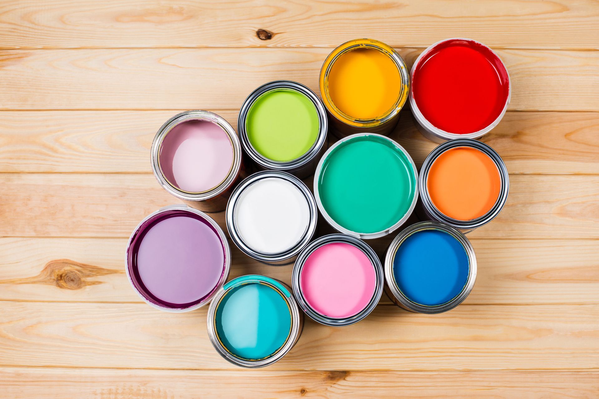 Open paint cans with various bright colors on wooden surface.