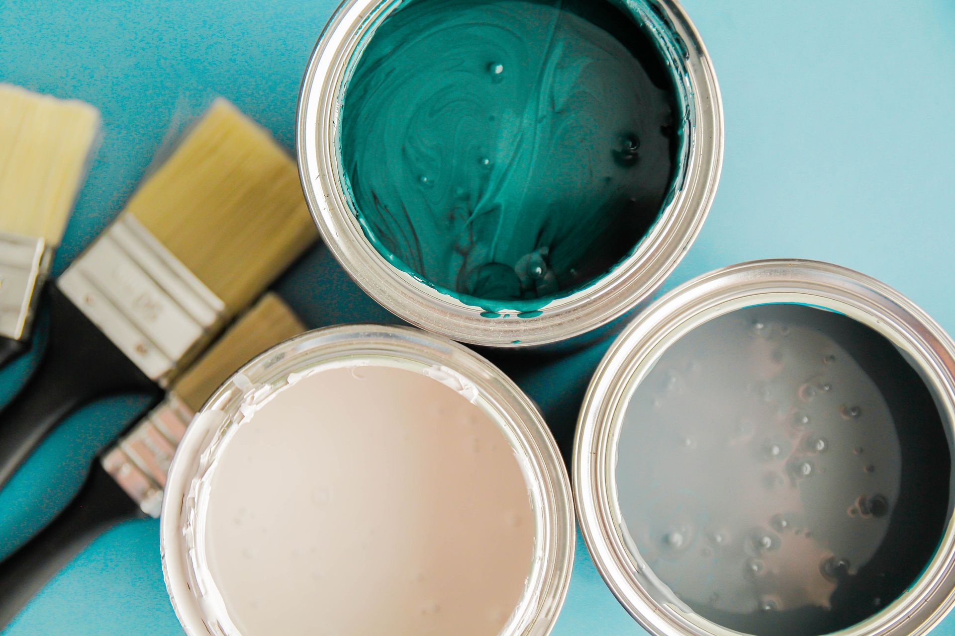 Three open paint cans with teal, peach, and gray paint, brushes alongside.