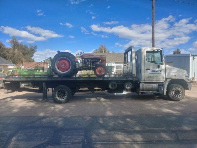 A tow truck is carrying a tractor on the back of it.
