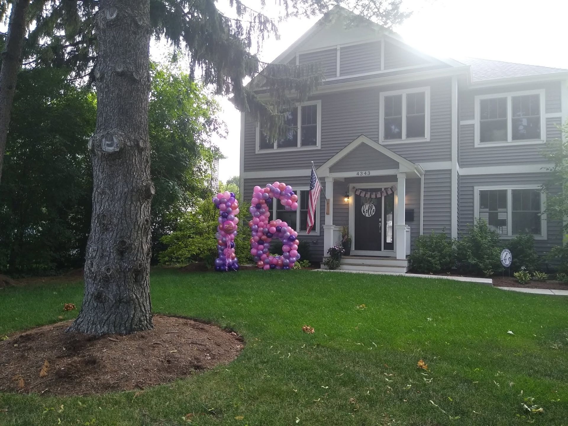 Two-story house with pink balloon decorations at the front entrance and a large tree in the yard