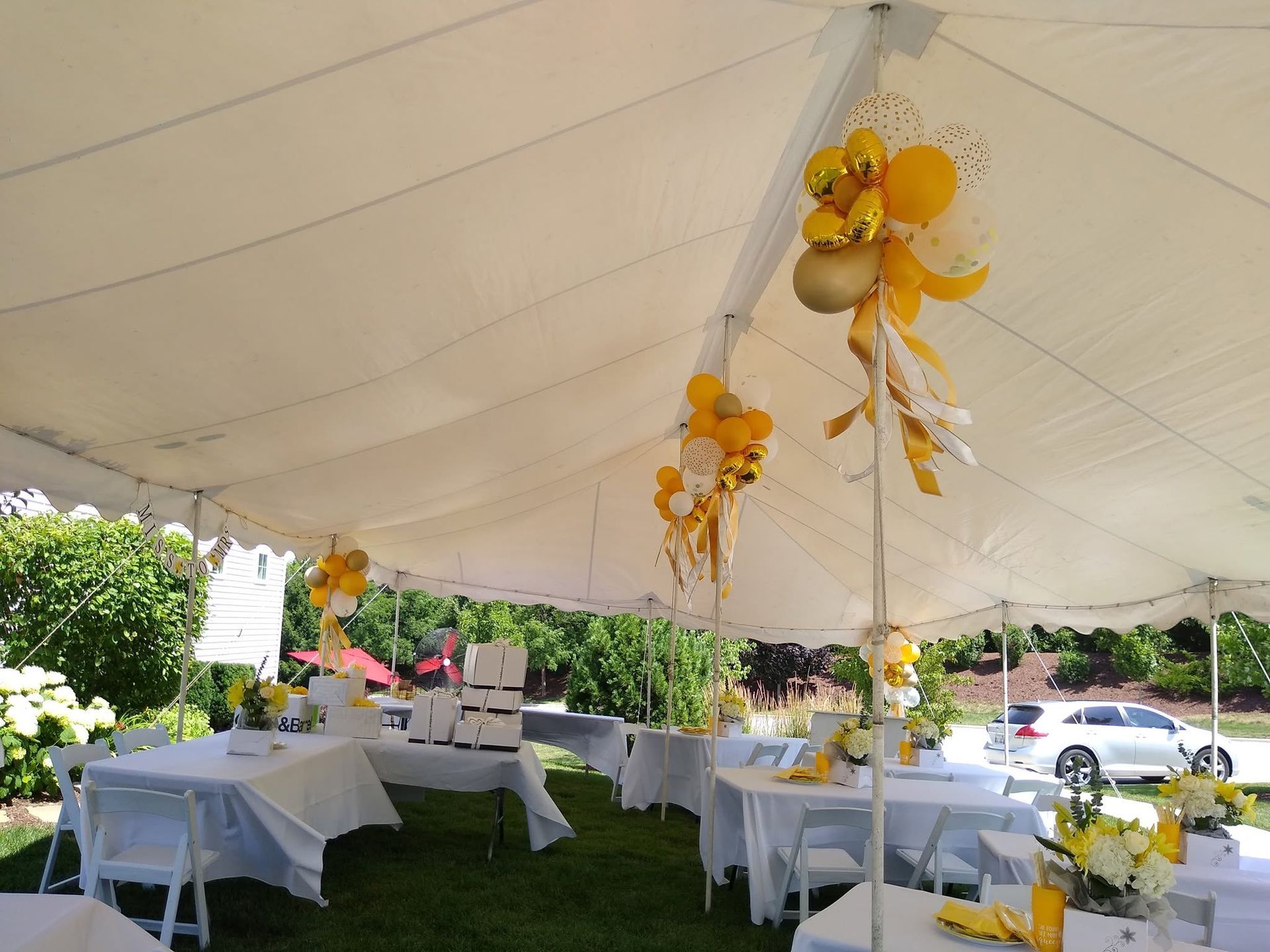 White tented outdoor reception with round tables, white tablecloths, and yellow floral decorations