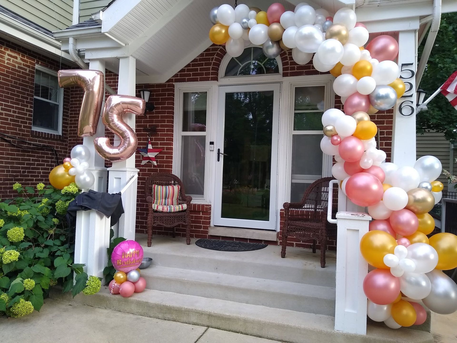 House porch decorated with white, gold, and pink balloon arch and a large rose-gold “5” balloon