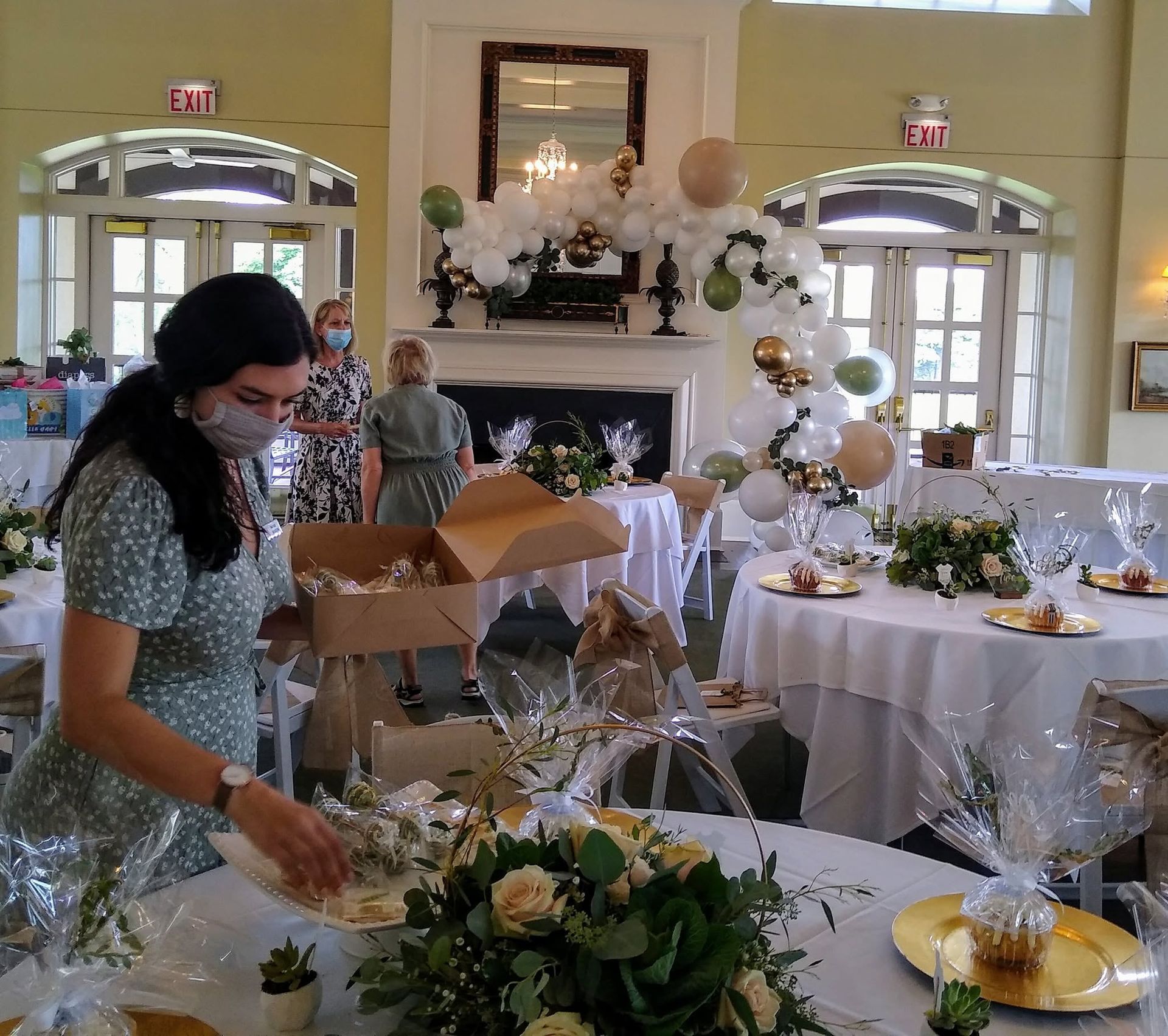 Woman arranging floral decor at a decorated banquet table in a bright event hall.