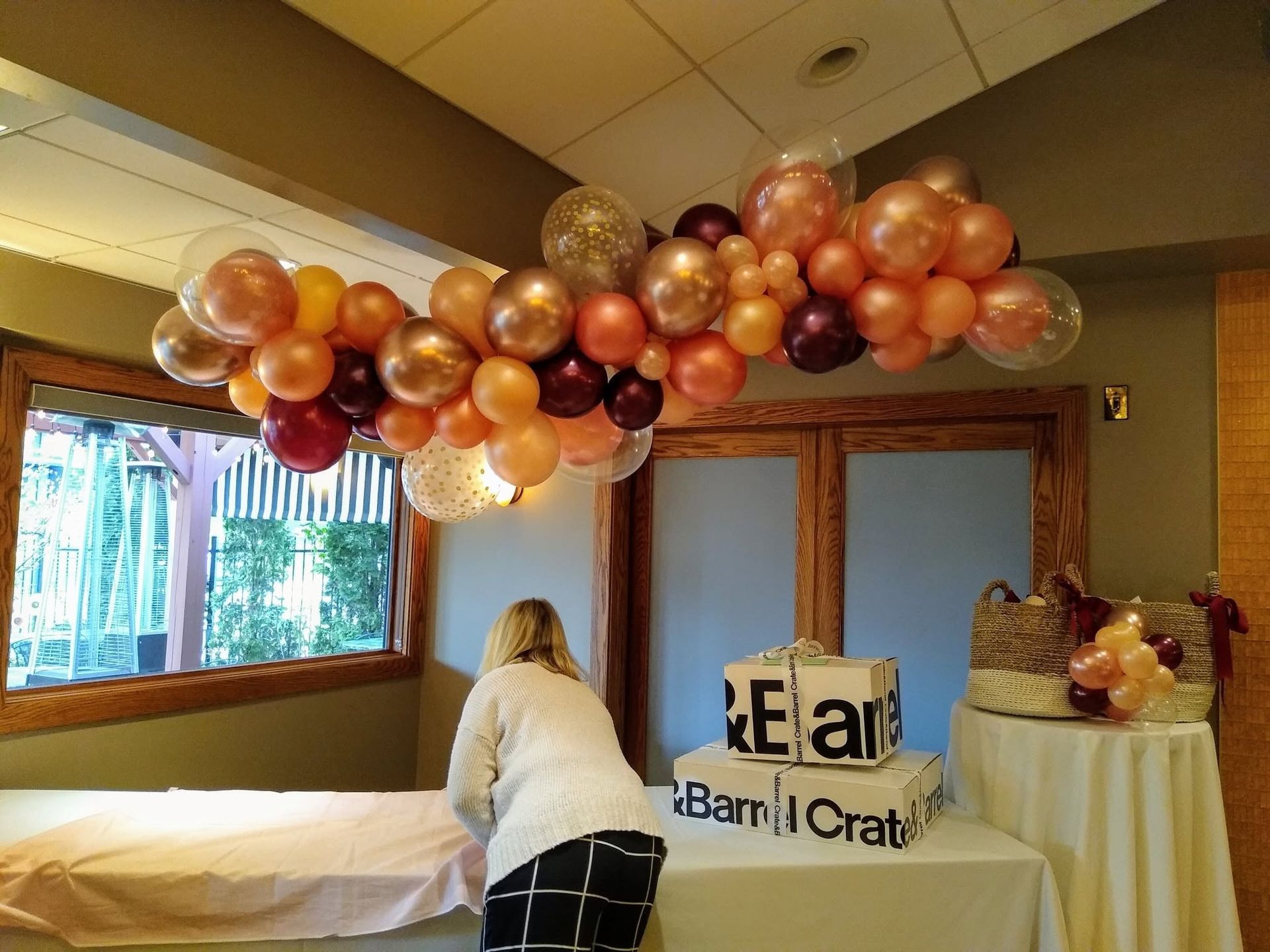 Decorated room with balloon garland, a person arranging a table, and a sign reading “Bamji Crate”