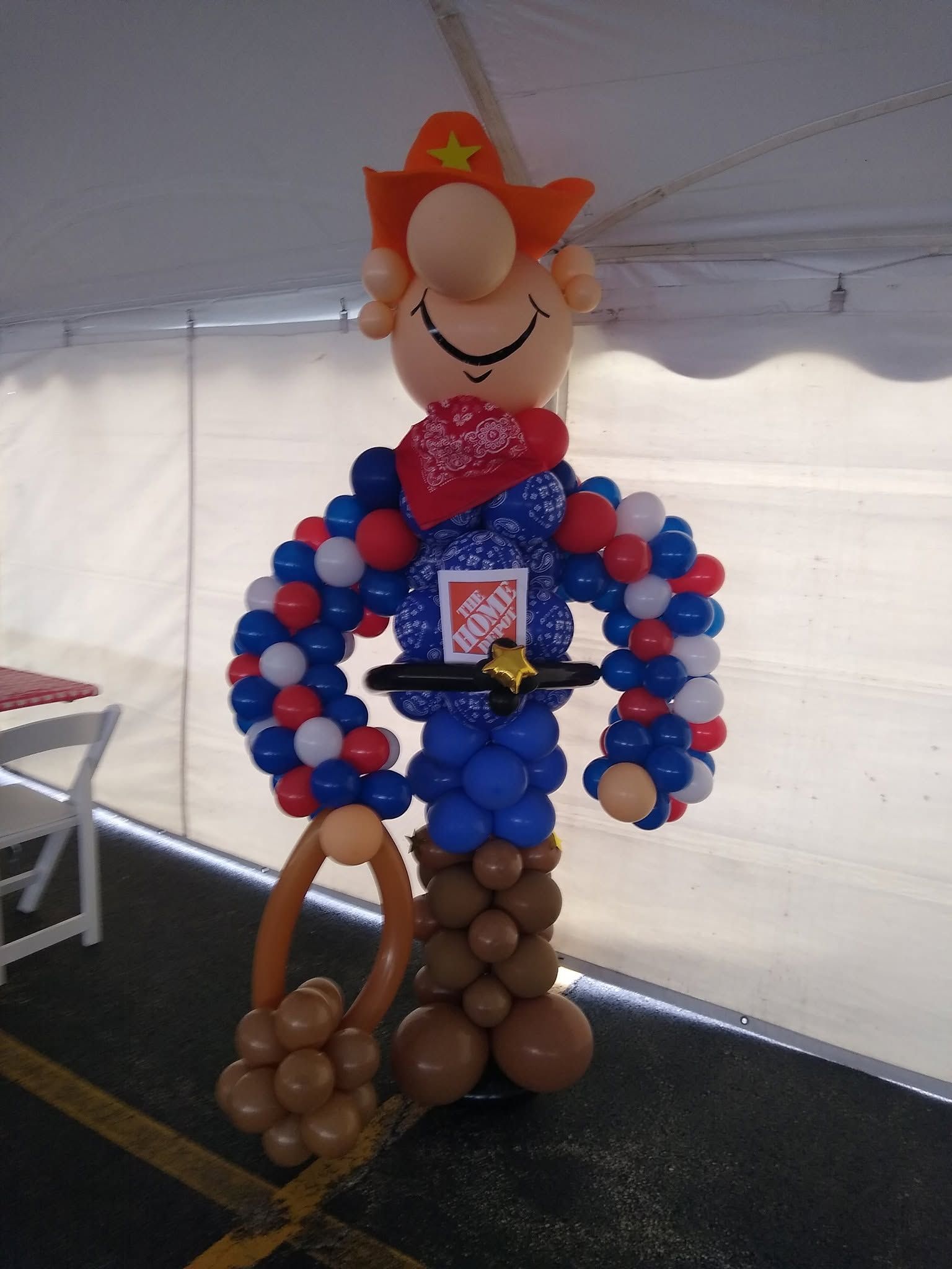 Balloon sculpture of a cowboy with red hat, blue and red body, holding a lasso at an indoor event.