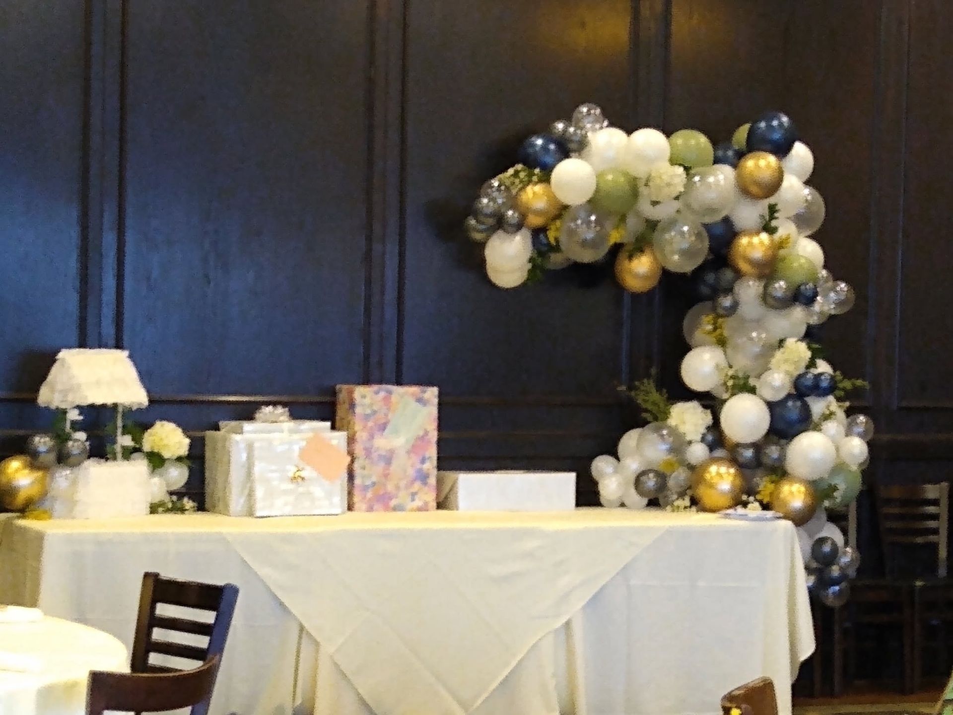 Balloon arch and decorated table at an event with dark wood paneling and a small lamp