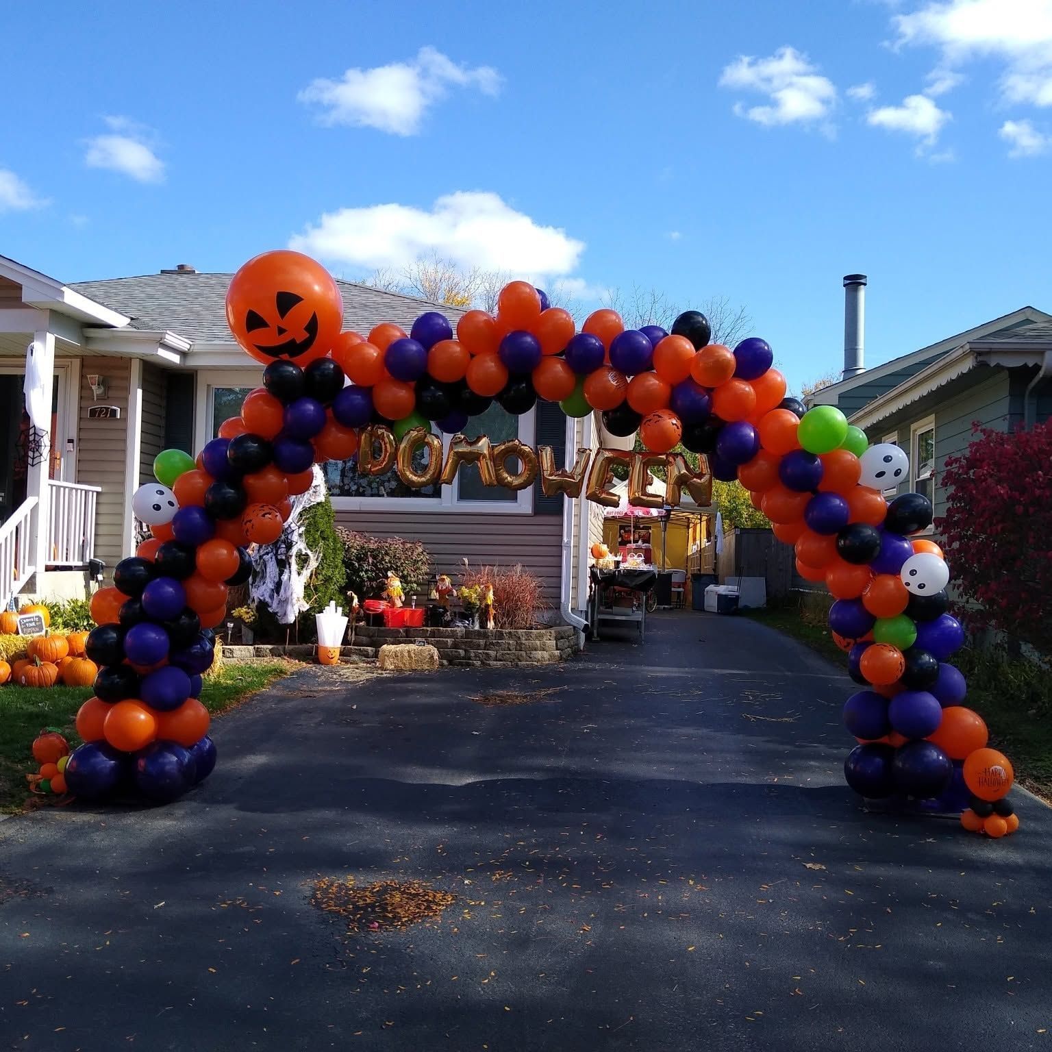 Halloween balloon arch over a driveway, decorated in orange, purple, and black with a jack-o'-lantern balloon